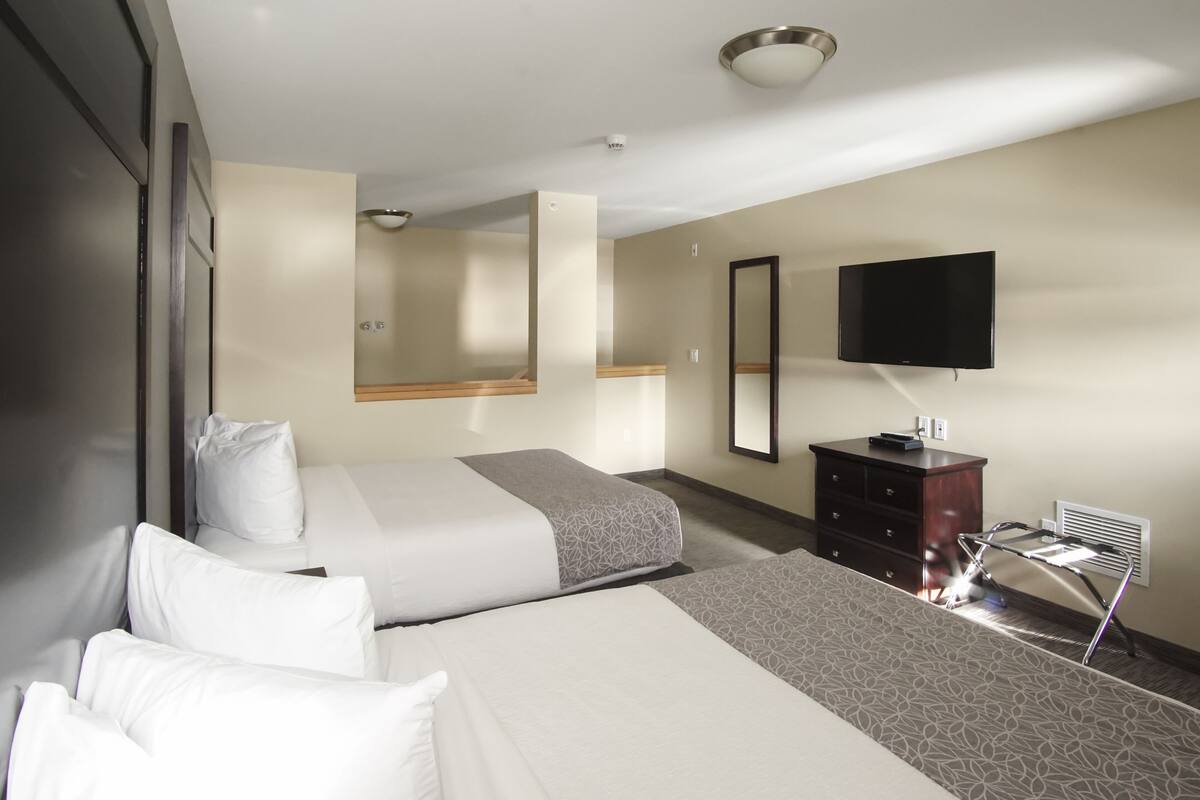 A hotel room with two beds, a flat-screen TV, a dresser, and a mirror.