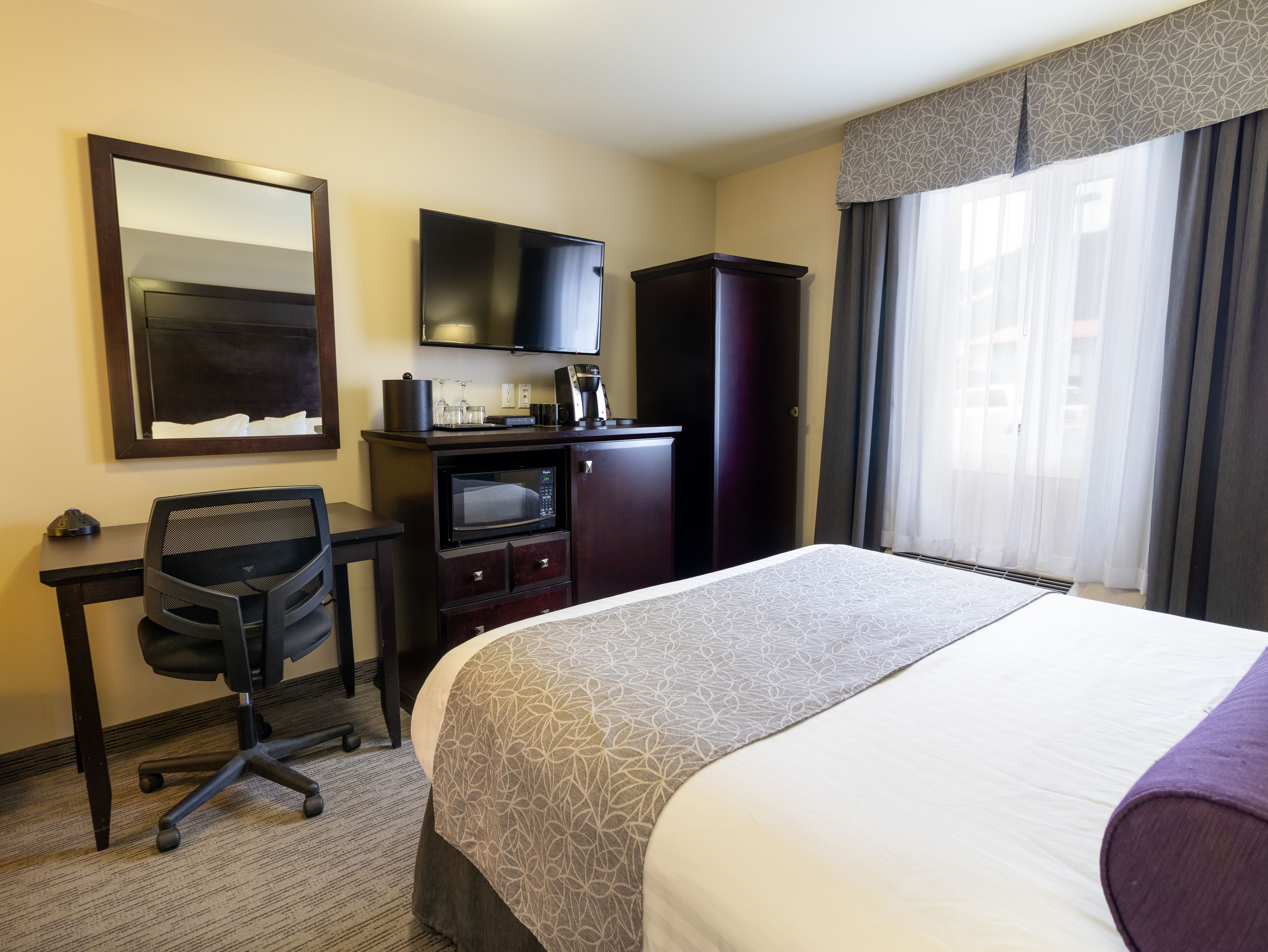 Habitación de hotel con cama, escritorio, silla, televisor, minibar y un amplio ventanal con cortinas.