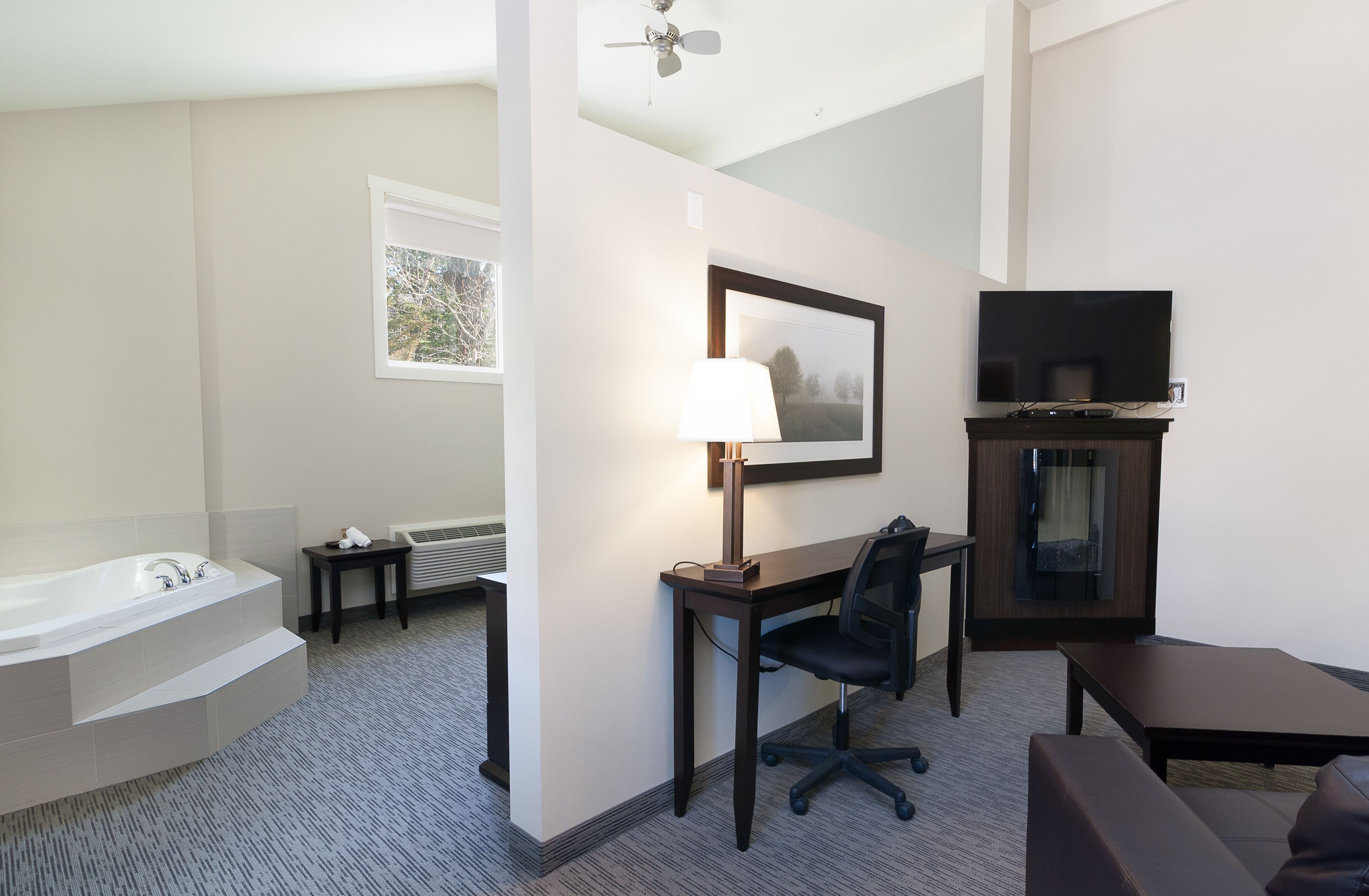 Habitación de hotel con bañera, escritorio, silla, televisor y chimenea.