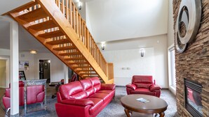 Un vestíbulo amplio con una escalera de madera, sofás de cuero rojo, una mesa de centro redonda de madera y una chimenea de piedra.