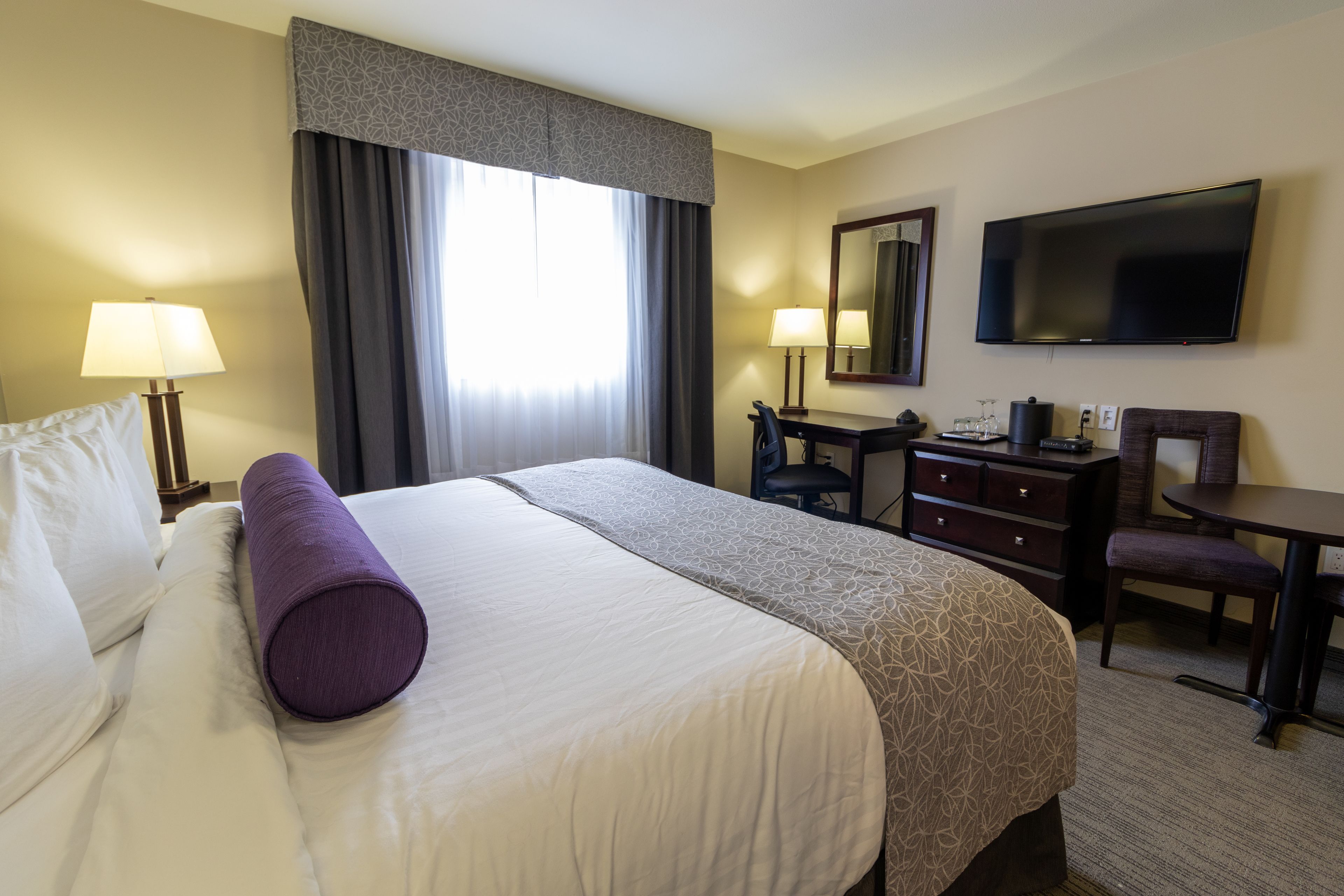 A hotel room with a bed, a desk, a chair, a TV, and a window with curtains.