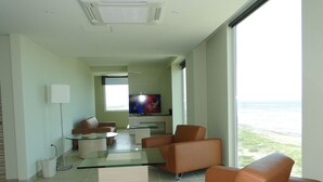 Una sala de estar moderna con una mesa de centro de vidrio, sofás de cuero, un televisor de pantalla plana y vista al océano.