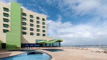 Un hotel con múltiples piscinas, vistas a la playa y un edificio grande con detalles en verde.