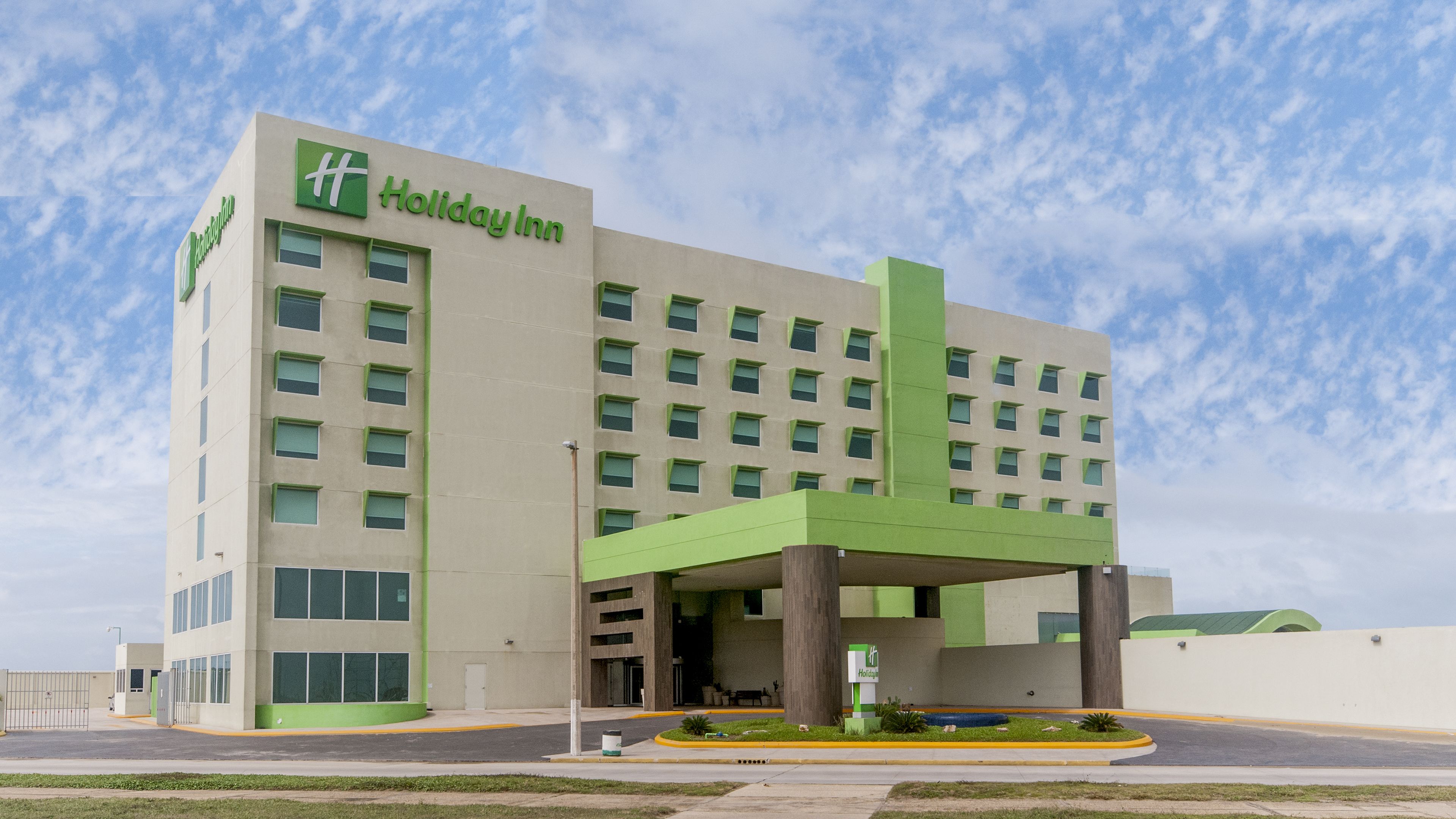 Een Holiday Inn hotelgebouw met een modern ontwerp, met een opvallende groene entree en meerdere ramen.