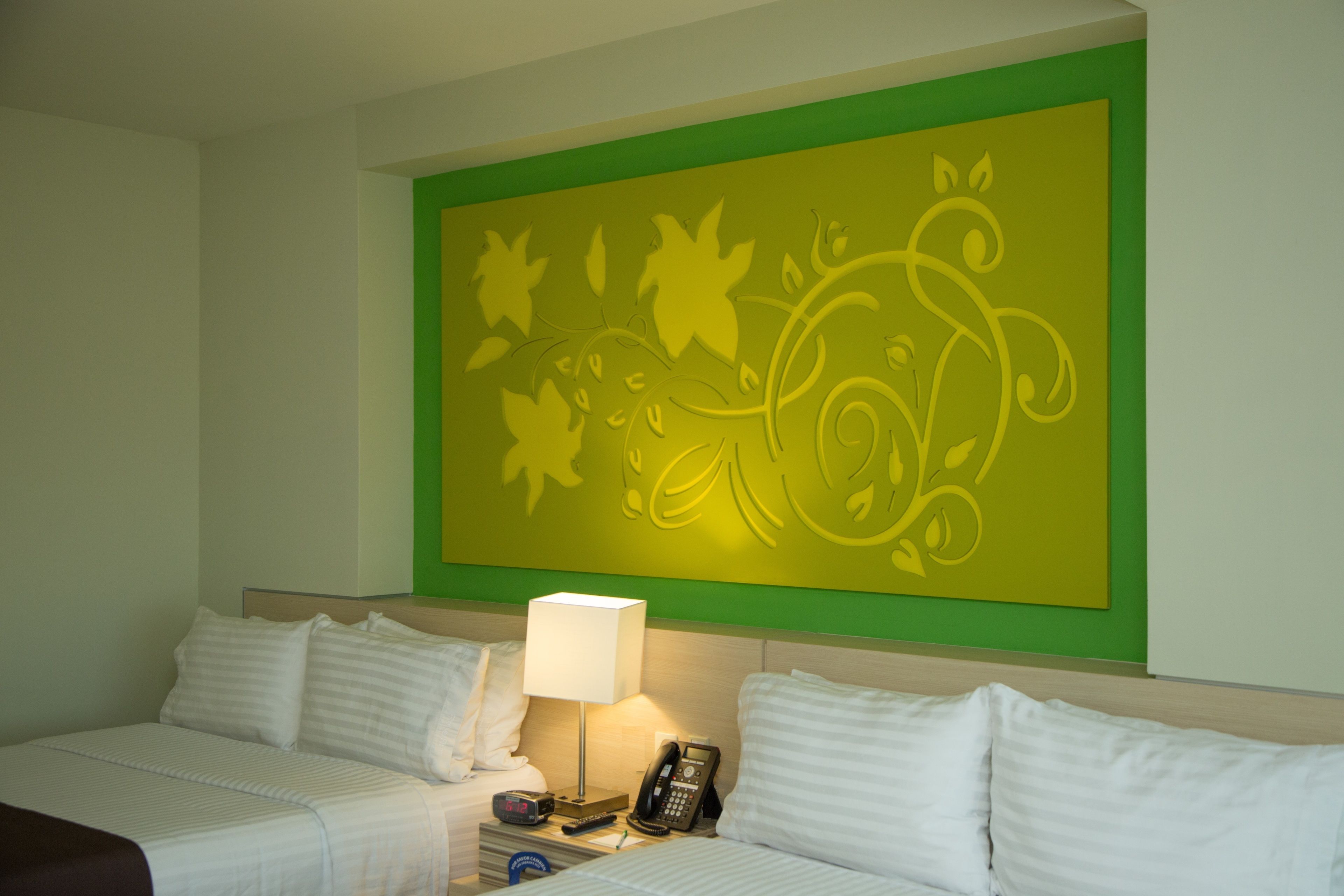 Habitación de hotel con dos camas, una mesita de noche con lámpara, teléfono y un adorno en la pared.