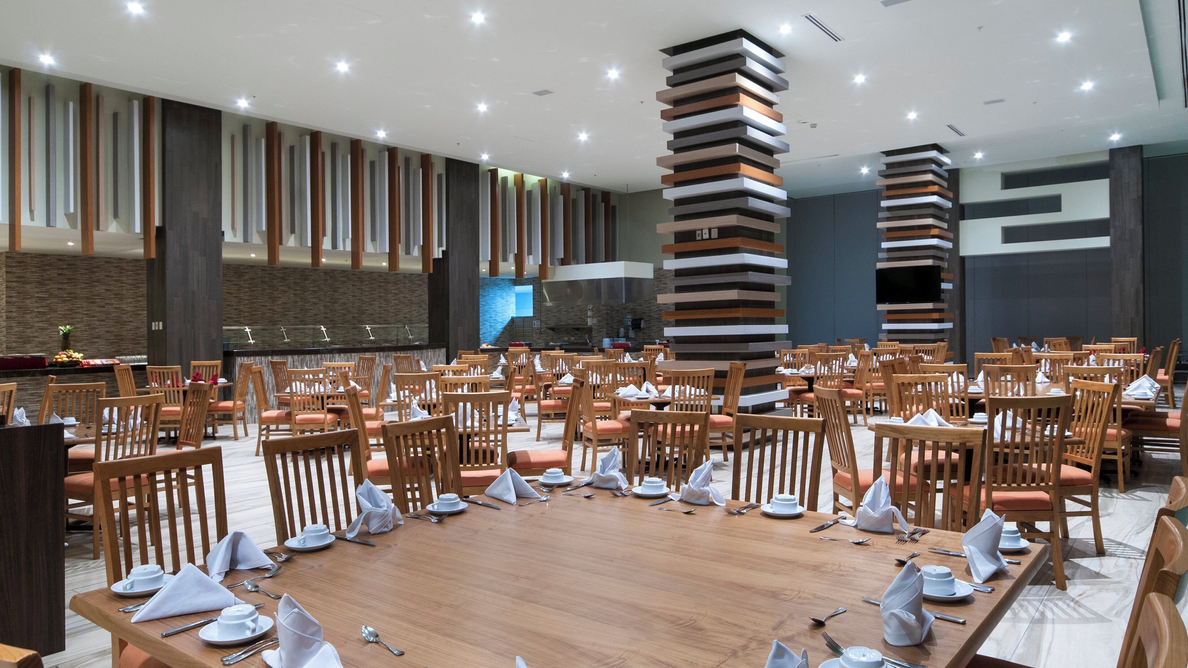 Un vaste espace dédié à la salle à manger, avec de nombreuses tables et chaises, un bar central et un aménagement intérieur moderne.