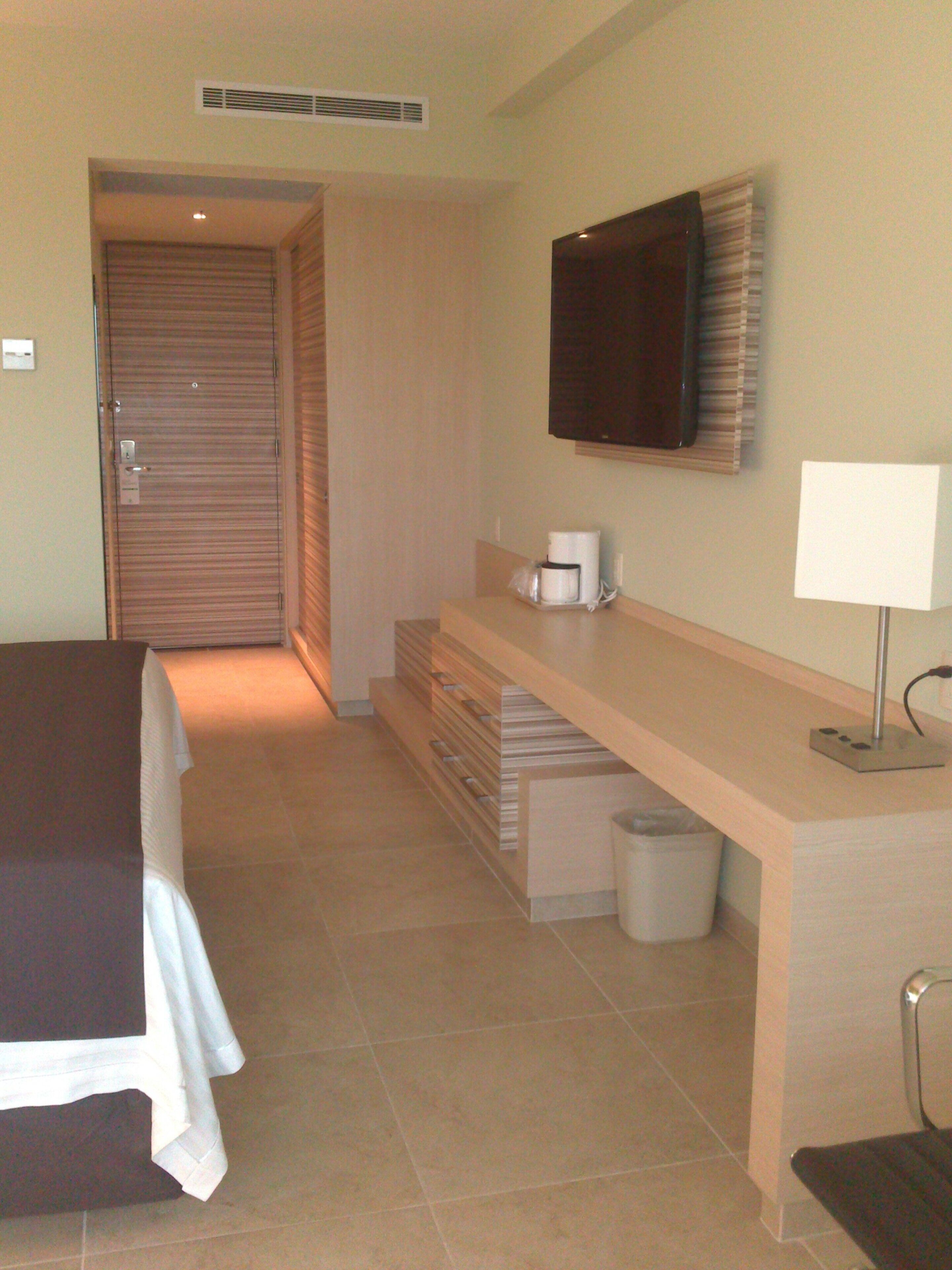 A hotel room with a bed, a desk with a lamp, a television, and a trash bin.
