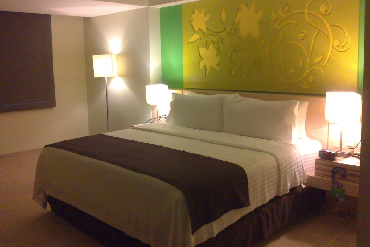 A hotel room with a bed, two bedside lamps, a nightstand, and a decorative wall panel.