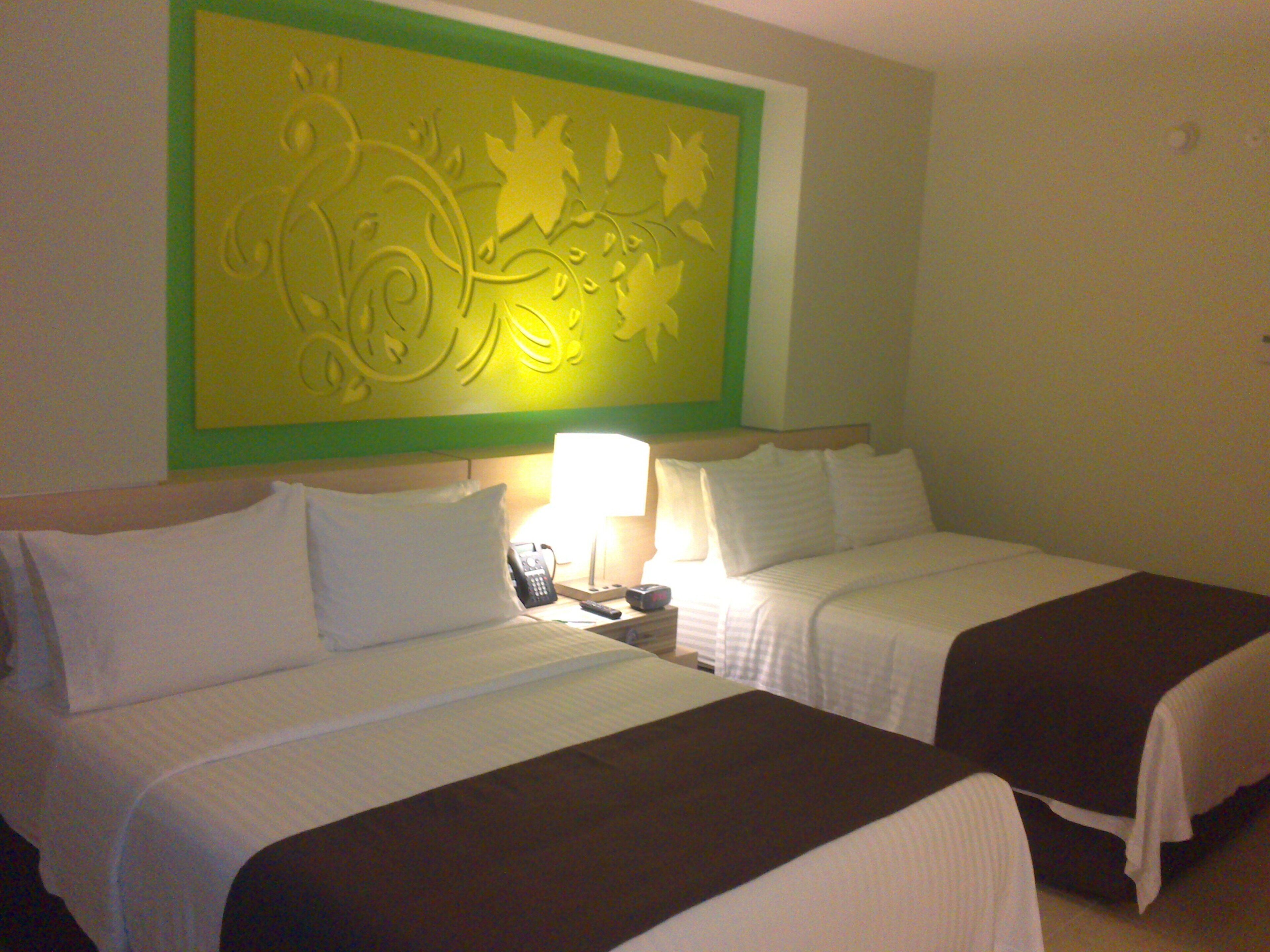 Habitación de hotel con dos camas, una mesita de noche con lámpara y un adorno en la pared sobre las camas.