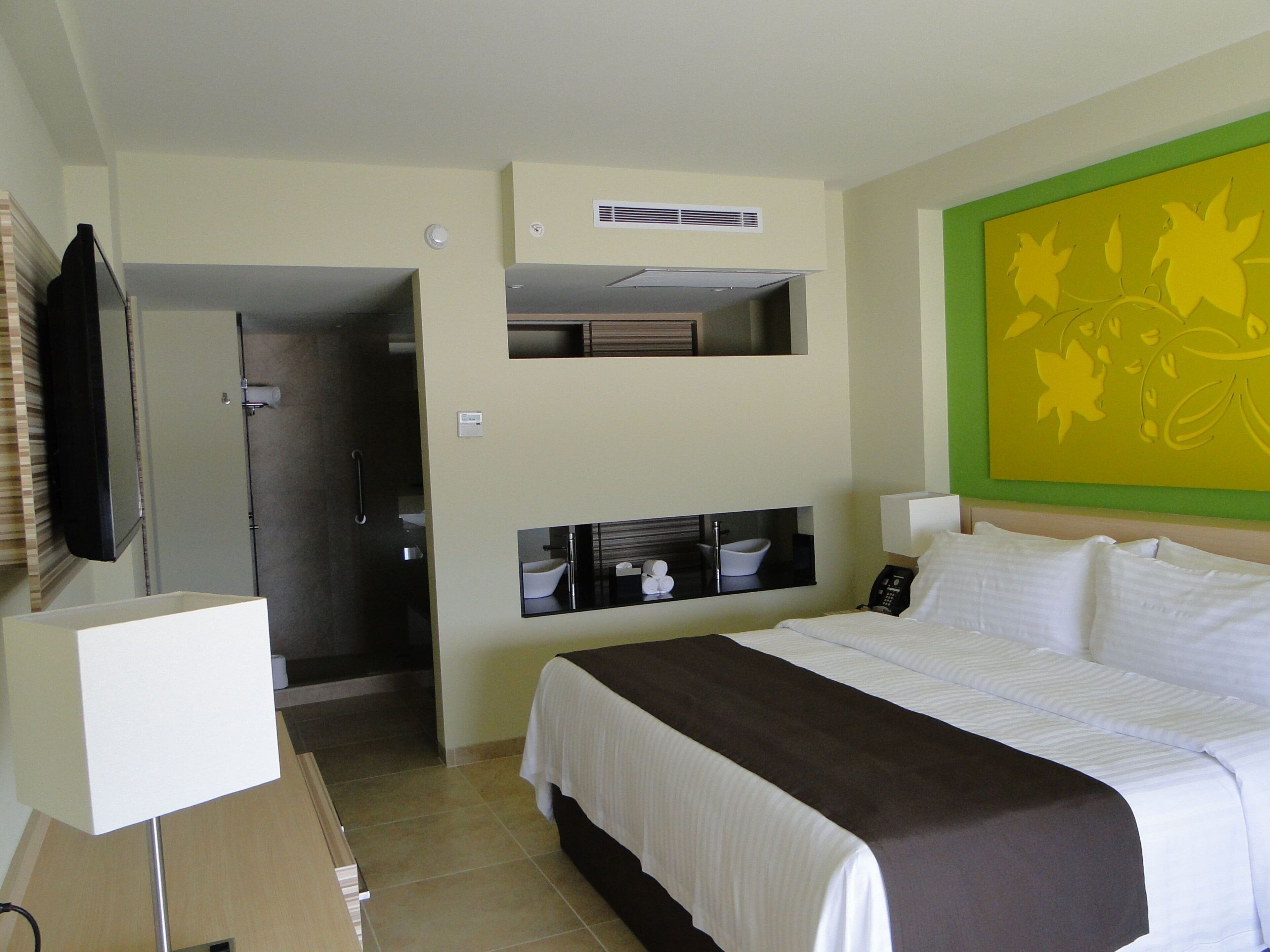 A hotel room with a bed, a television, a bathroom, and a green wall decoration.