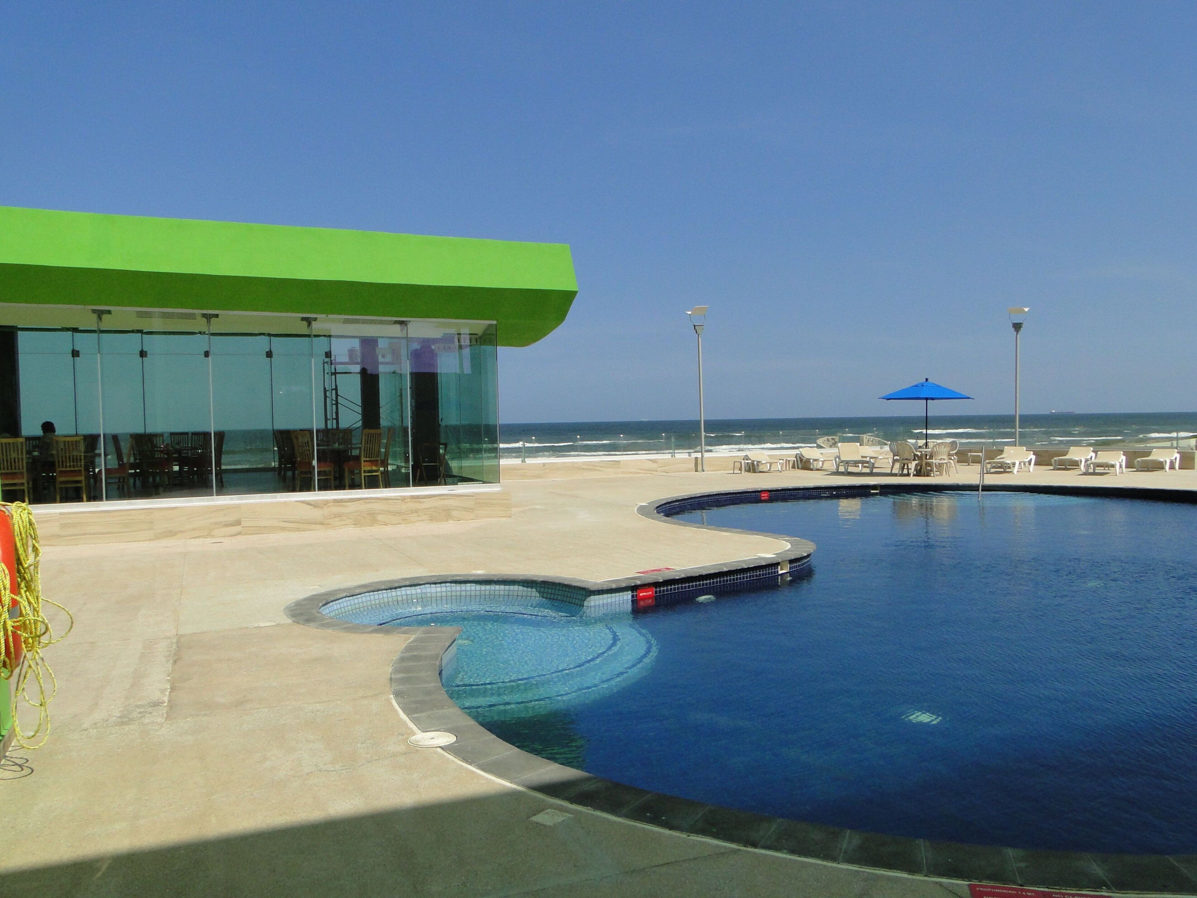 Ein Poolbereich mit geschwungenem Design, ein Gebäude mit Gründach und Blick auf den Ozean.