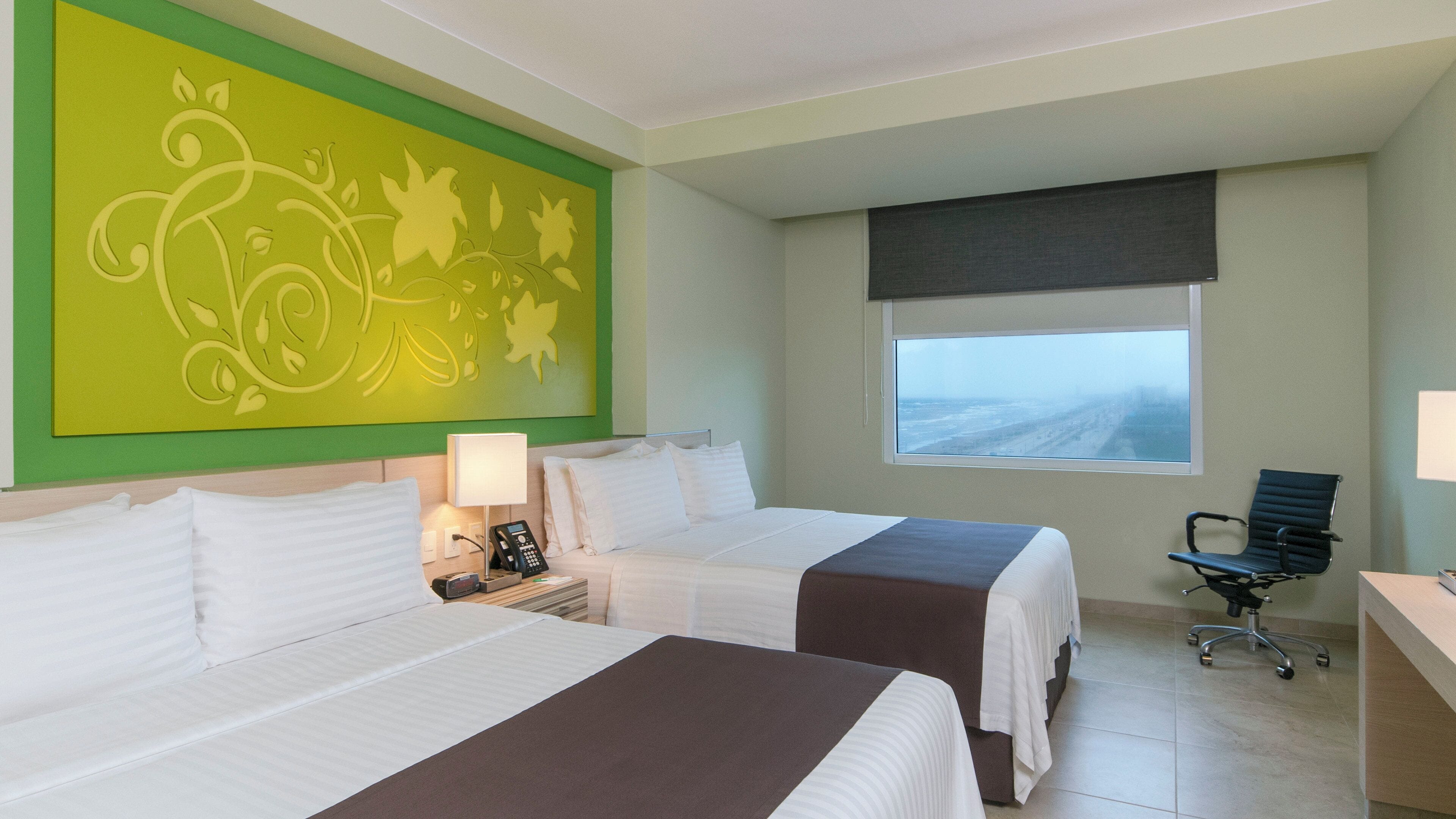 A hotel room with two beds, a desk, a chair, a telephone, and a window with a view.