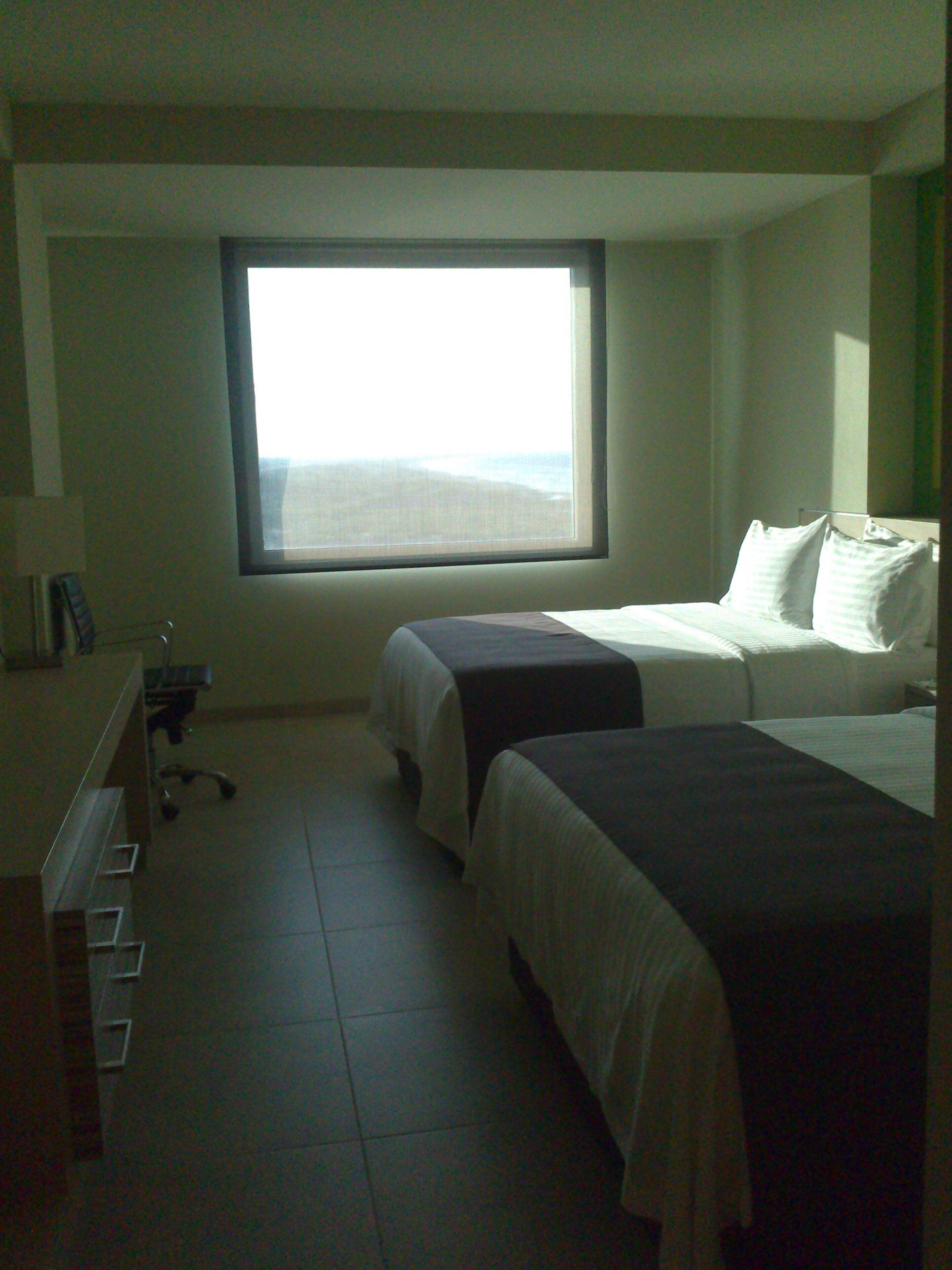 A hotel room with two beds, a desk, and a window with a view of the beach.