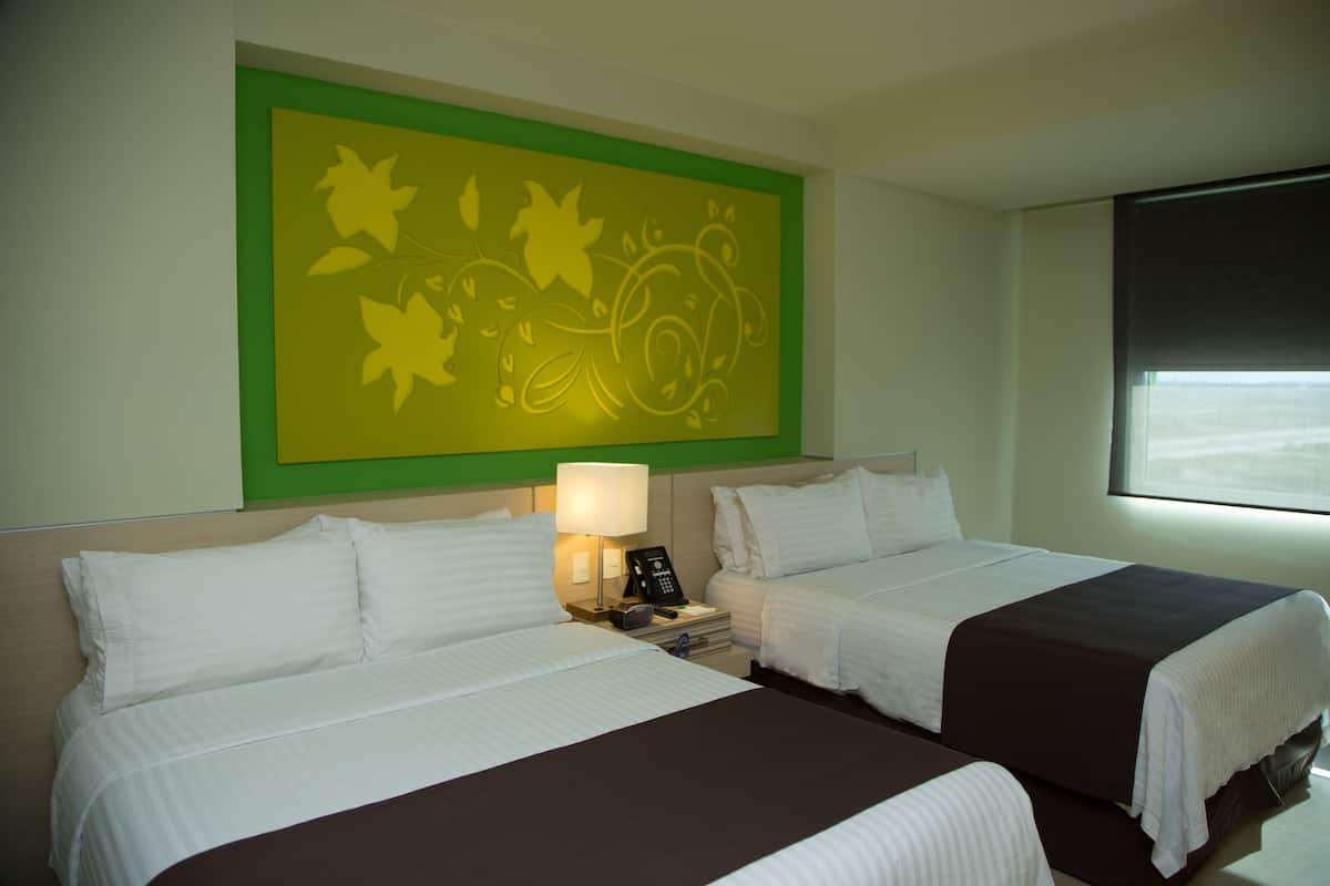A hotel room with two beds, a nightstand with a lamp, and a wall art piece.