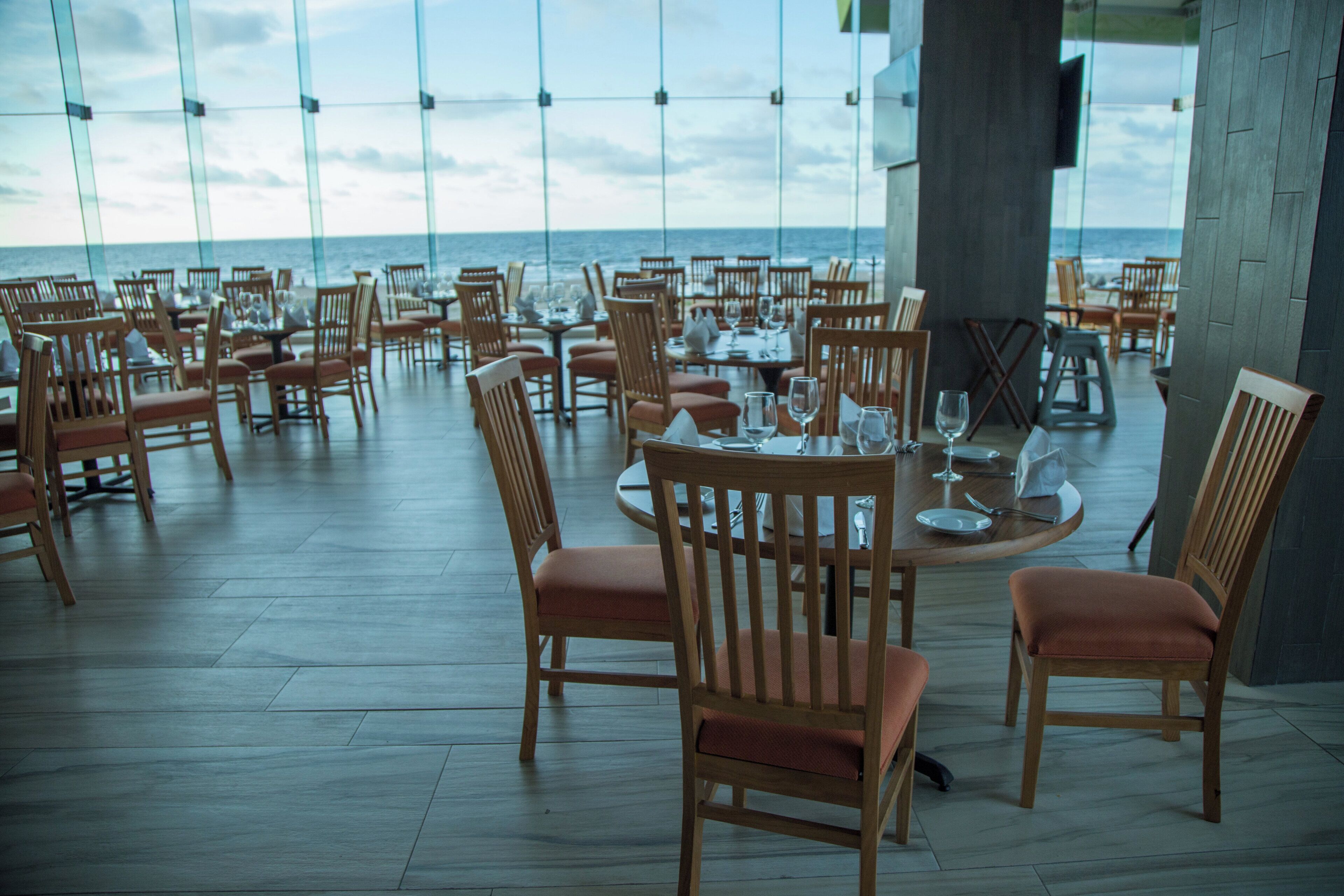 Un restaurant avec des tables rondes et des chaises en bois, offrant une vue sur l’océan.