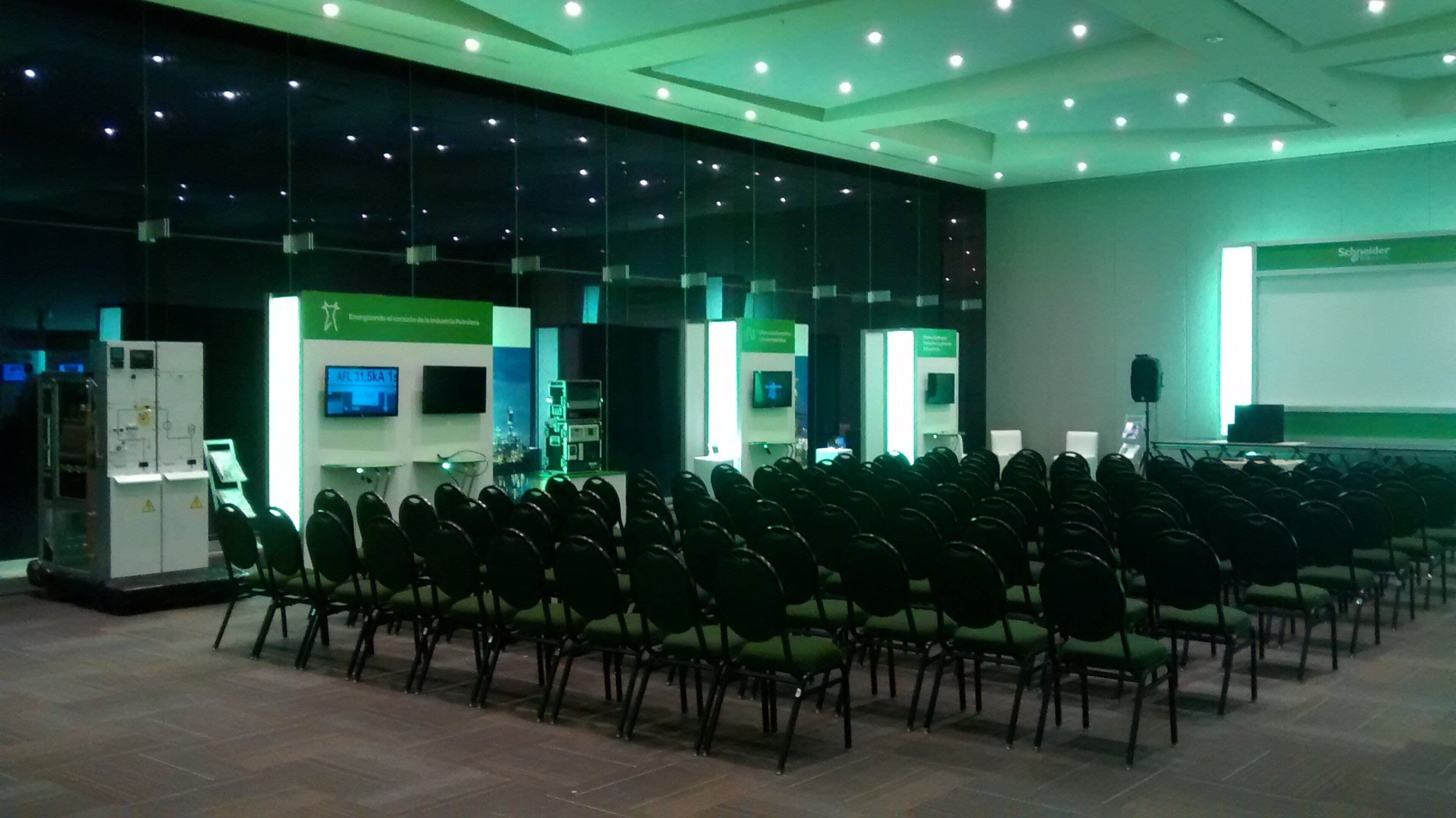 A conference room with rows of chairs, a presentation screen, and a stage area with a speaker.