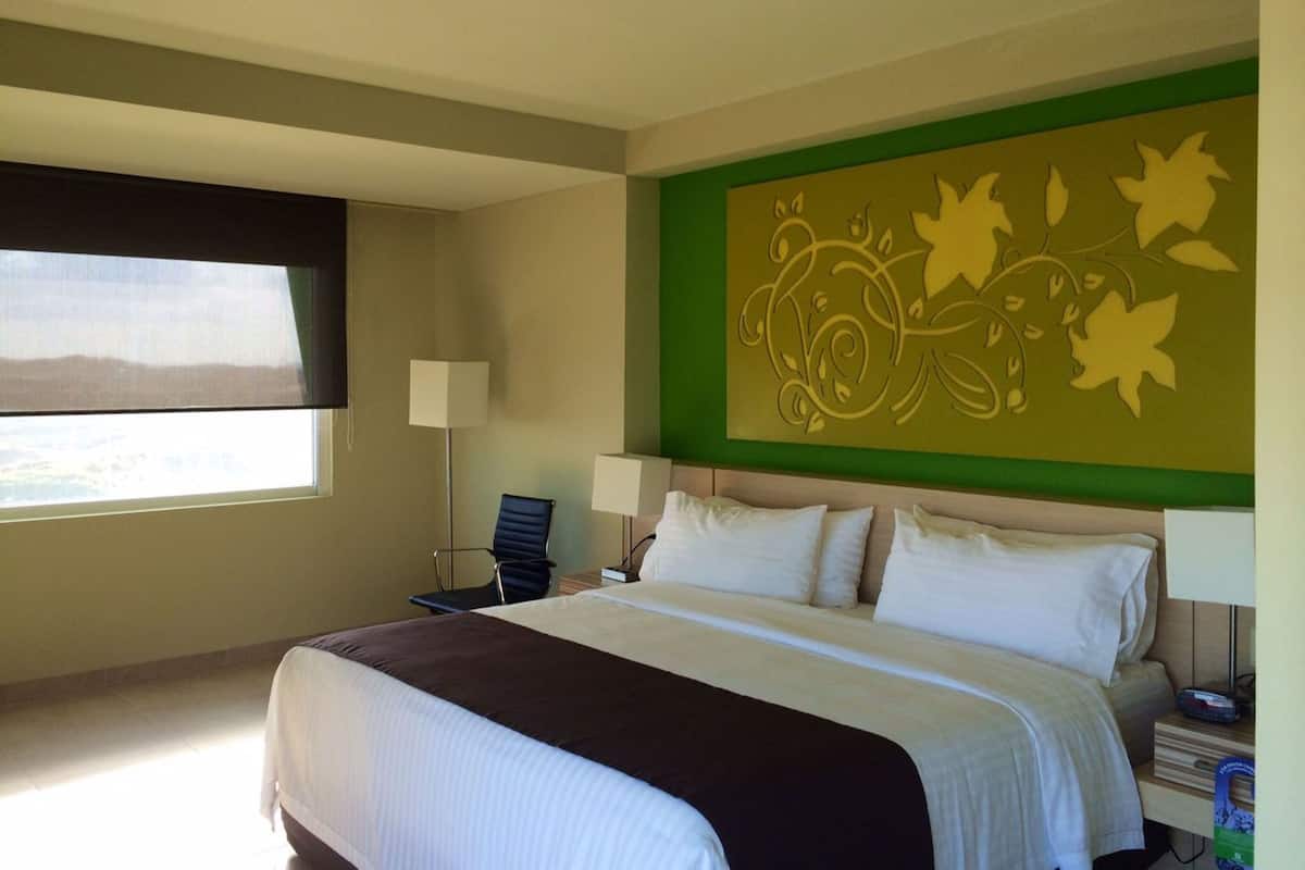 A hotel room with a large bed, a desk, a chair, and a window with a view.