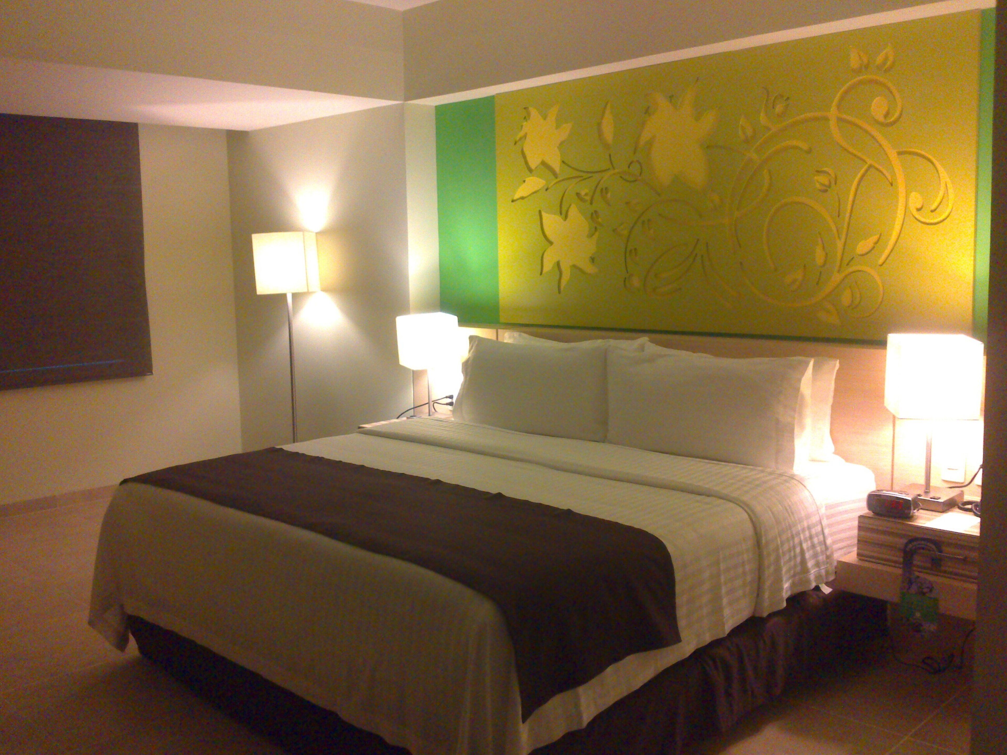Una habitación de hotel con una cama, dos lámparas de noche, una mesita de noche y una pared con un diseño de hojas.