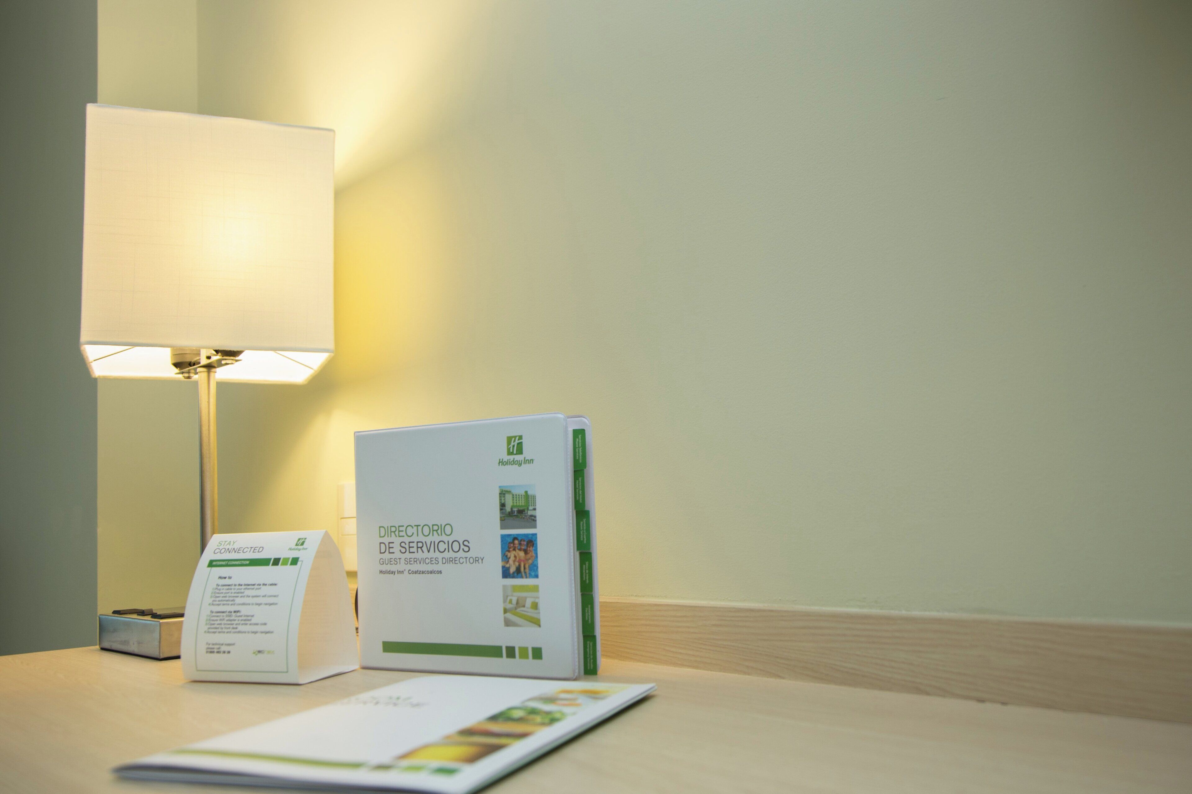 A hotel room with a directional services guest services directory, a stay connected sign, and a lamp.