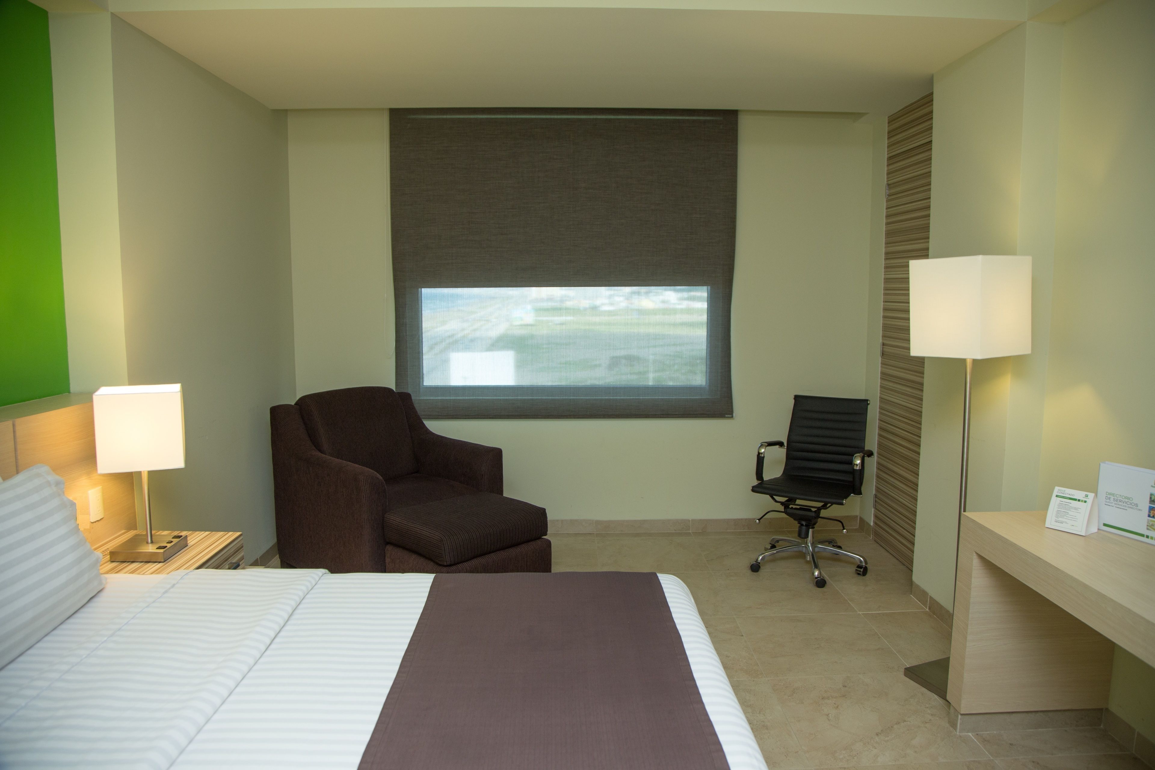 A hotel room with a bed, two chairs, a desk, and a window with a view.