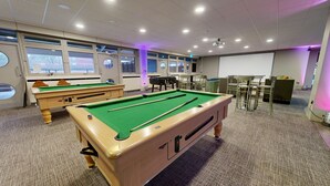 A pool table with a green felt surface, a pool cue, and a billiard ball. There are two pool tables, chairs, and a projector screen in the room. - Yarnfield Park Training Centre (Stone)