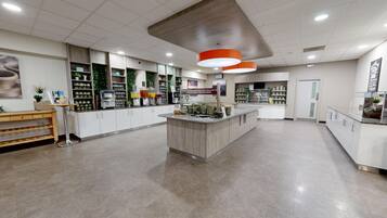A clean, modern reception area with a central counter, shelves with various items, and a sign reminding not to waste food.