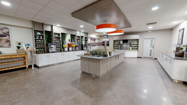 Un área de recepción limpia y moderna, con un mostrador central, estanterías con diversos artículos y un cartel que recuerda no desperdiciar alimentos.