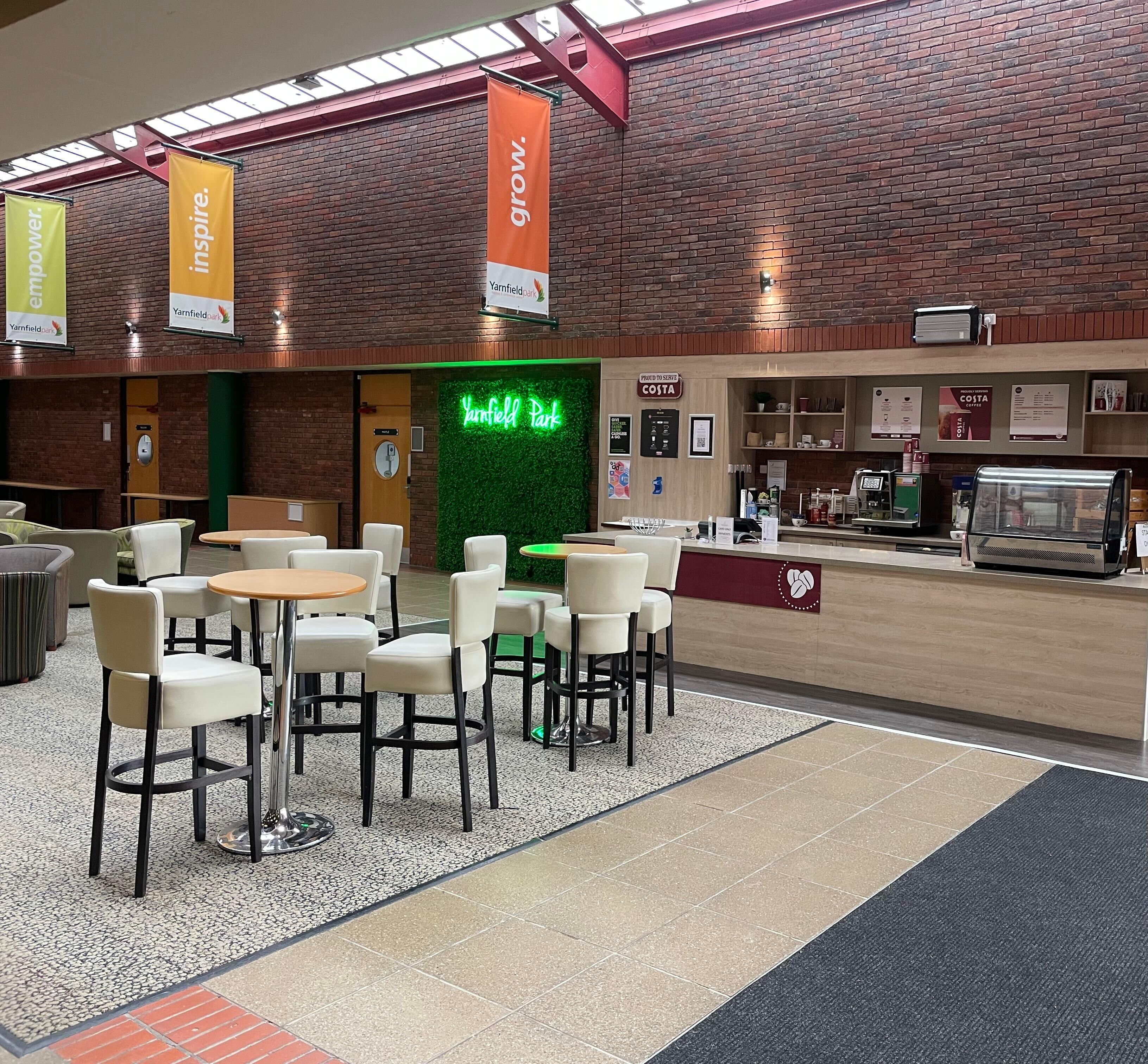 A cafe interior with tables and chairs, a counter with a coffee machine, and a neon sign.