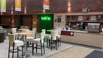 A cafe interior with tables and chairs, a counter with a coffee machine, and a neon sign.