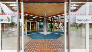 The entrance of Yarnfield Park training & conference centre with glass doors, a tiled floor, and a ceiling with a wooden lattice design. - Yarnfield Park Training Centre (Stone)