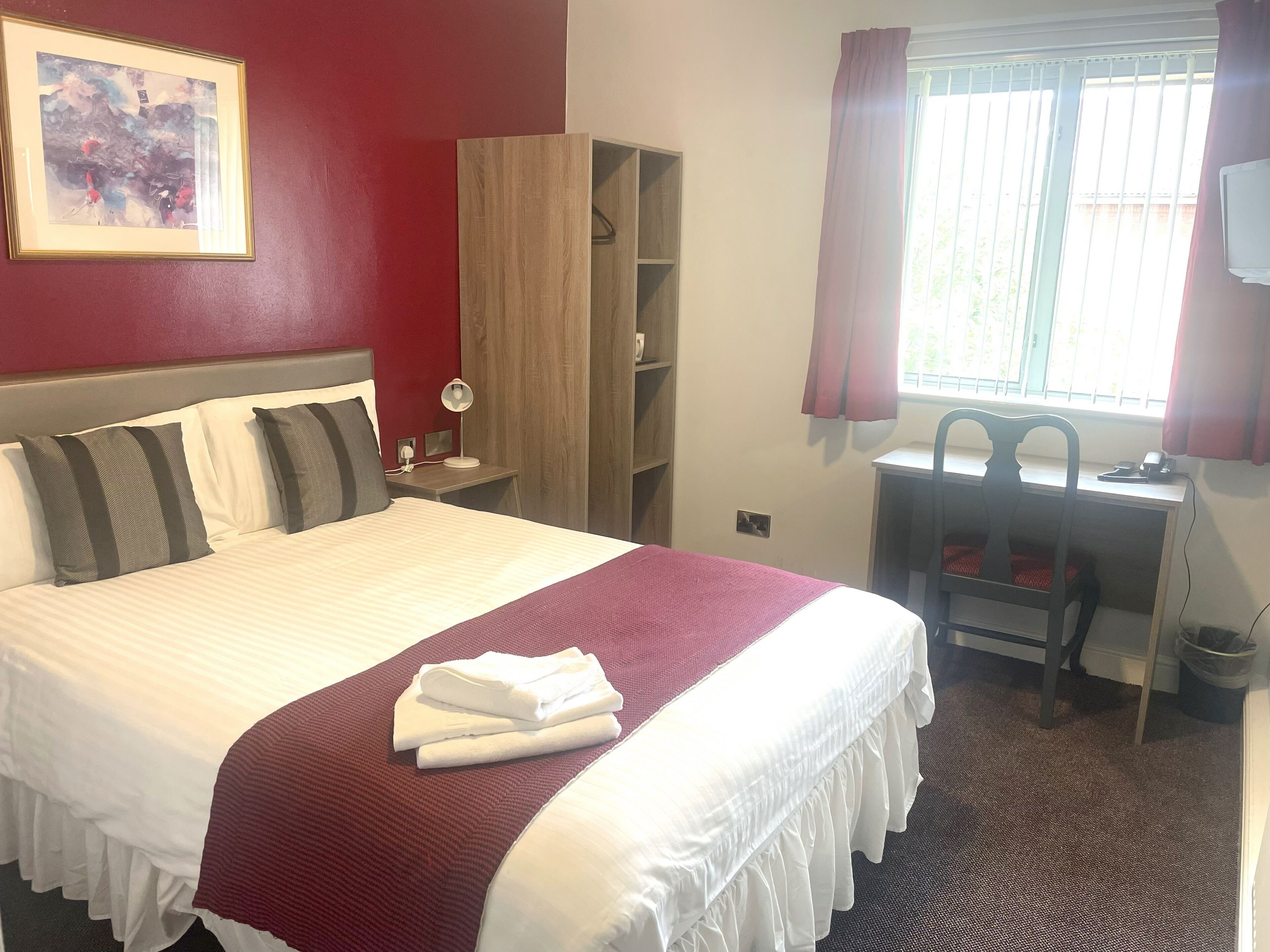 A hotel room with a bed, a desk, a chair, a wardrobe, and a window with curtains.