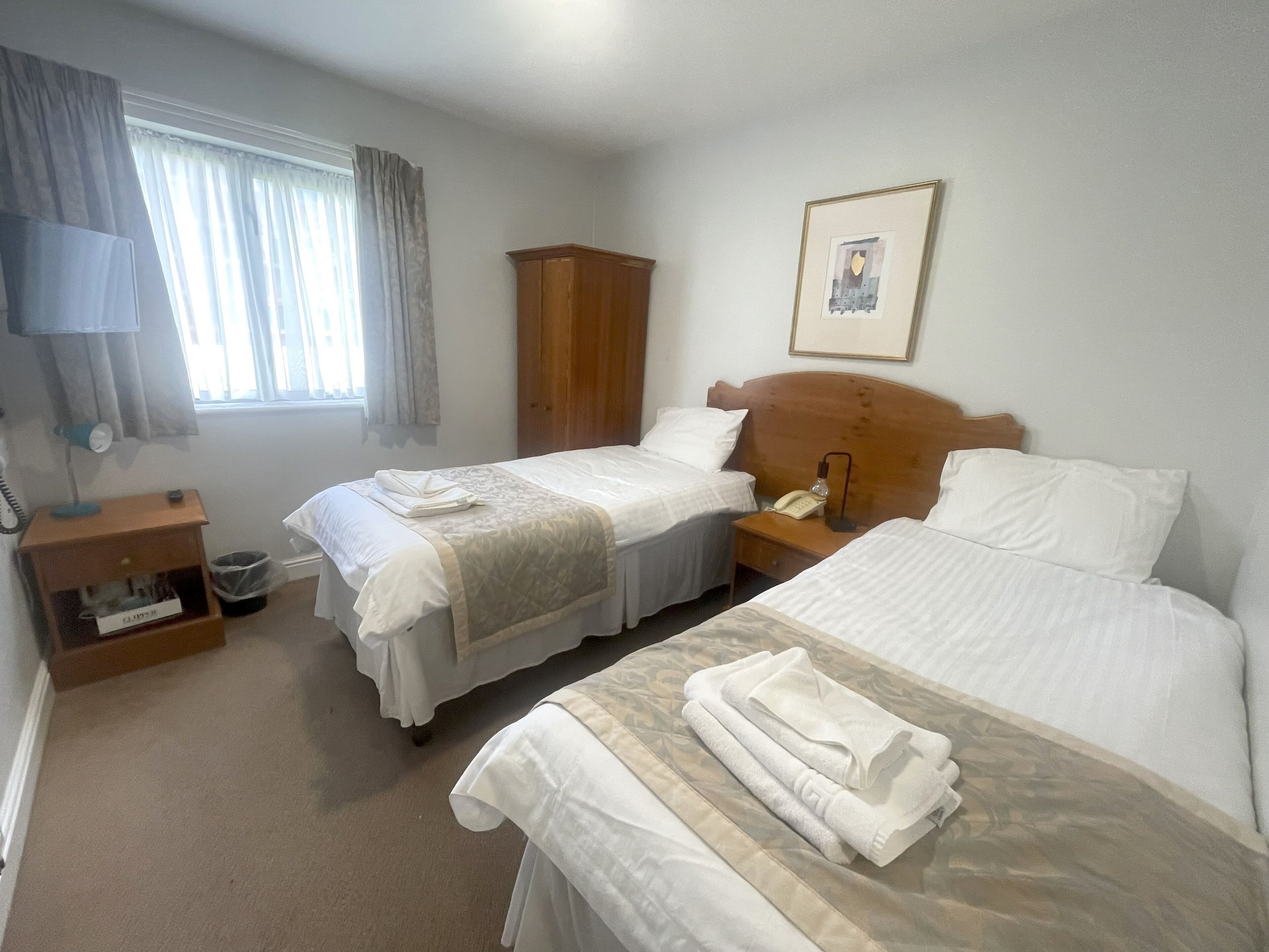 Ein Hotelzimmer mit zwei Betten, einem Holzschrank, einem Nachttisch mit Lampe und einem gerahmten Bild an der Wand.