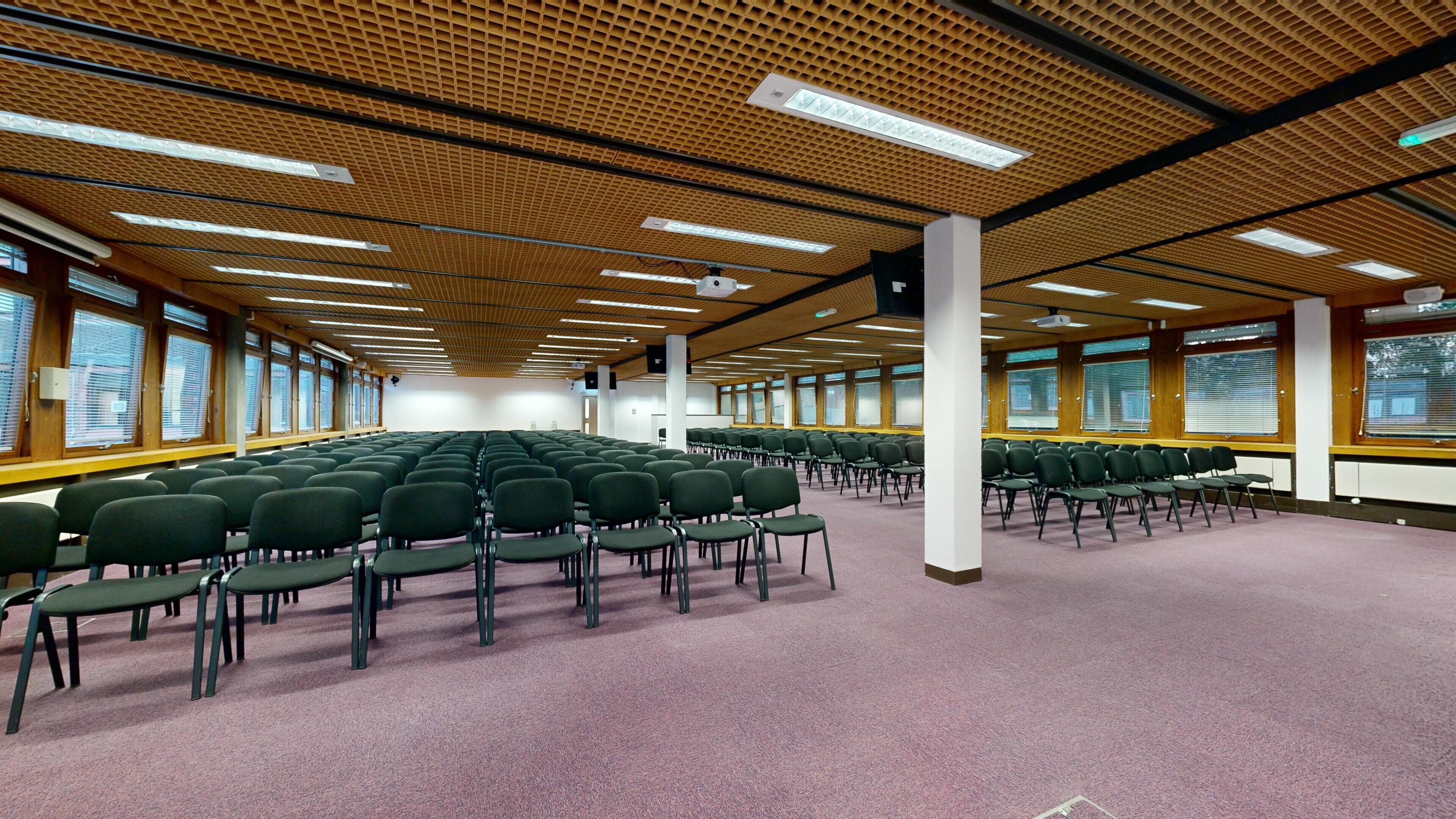 A conference room with rows of chairs, large windows, and a wooden ceiling.