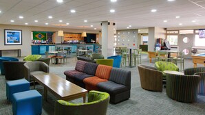 A spacious lounge area with multiple seating options including sofas, chairs, and tables. A bar area with a variety of beverages is visible in the background. - Yarnfield Park Training Centre (Stone)