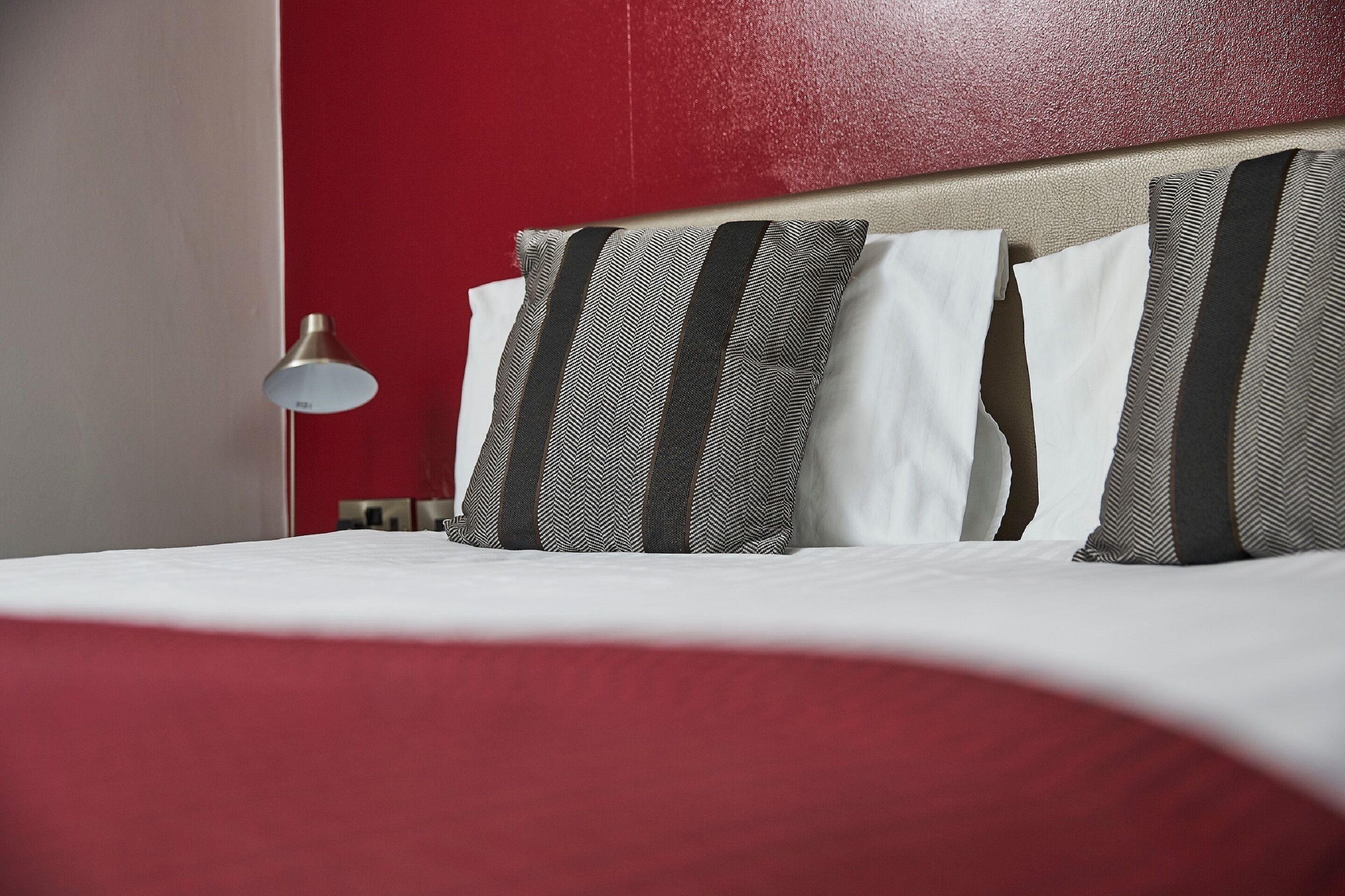 Ein Hotelzimmer mit einem Bett, Kissen, einer Lampe und einer roten Wand.