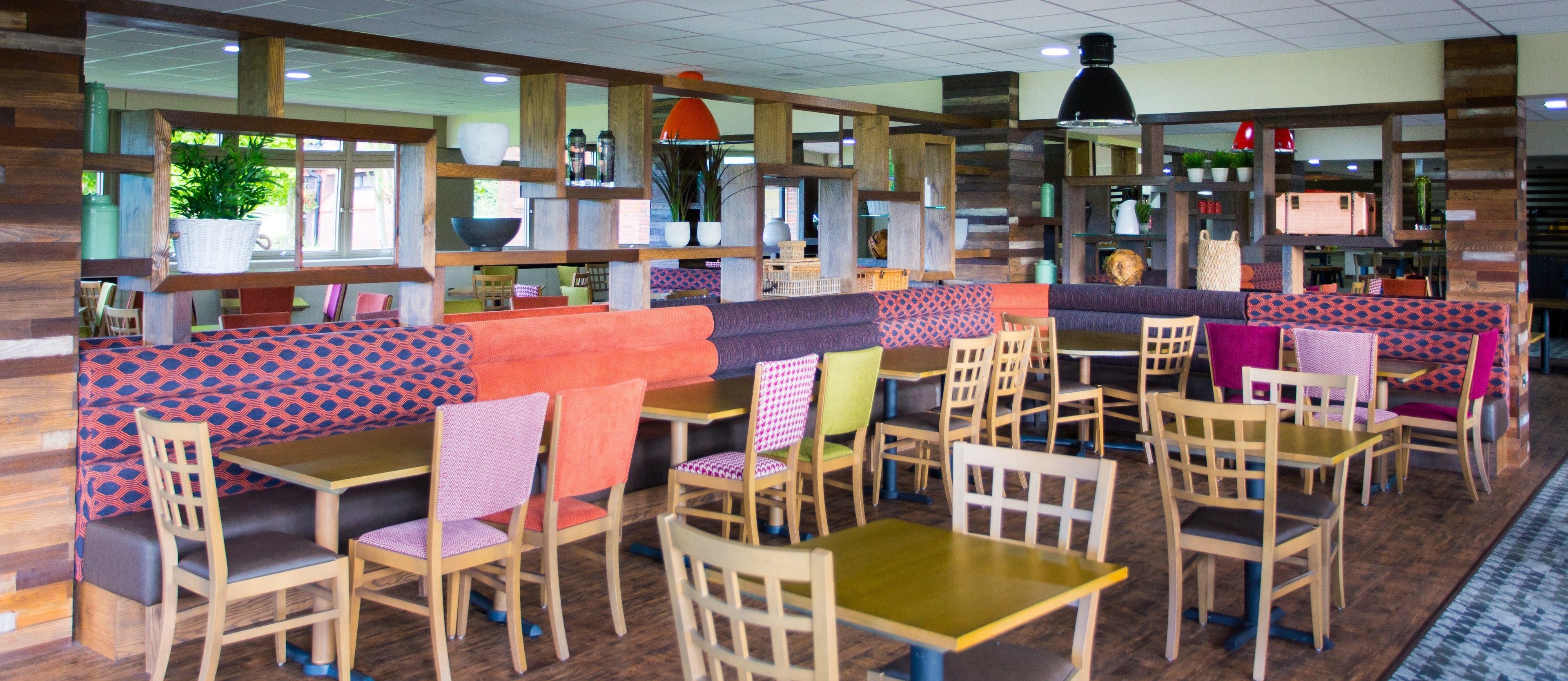 A restaurant with booths and tables, wooden flooring, and a variety of chairs.