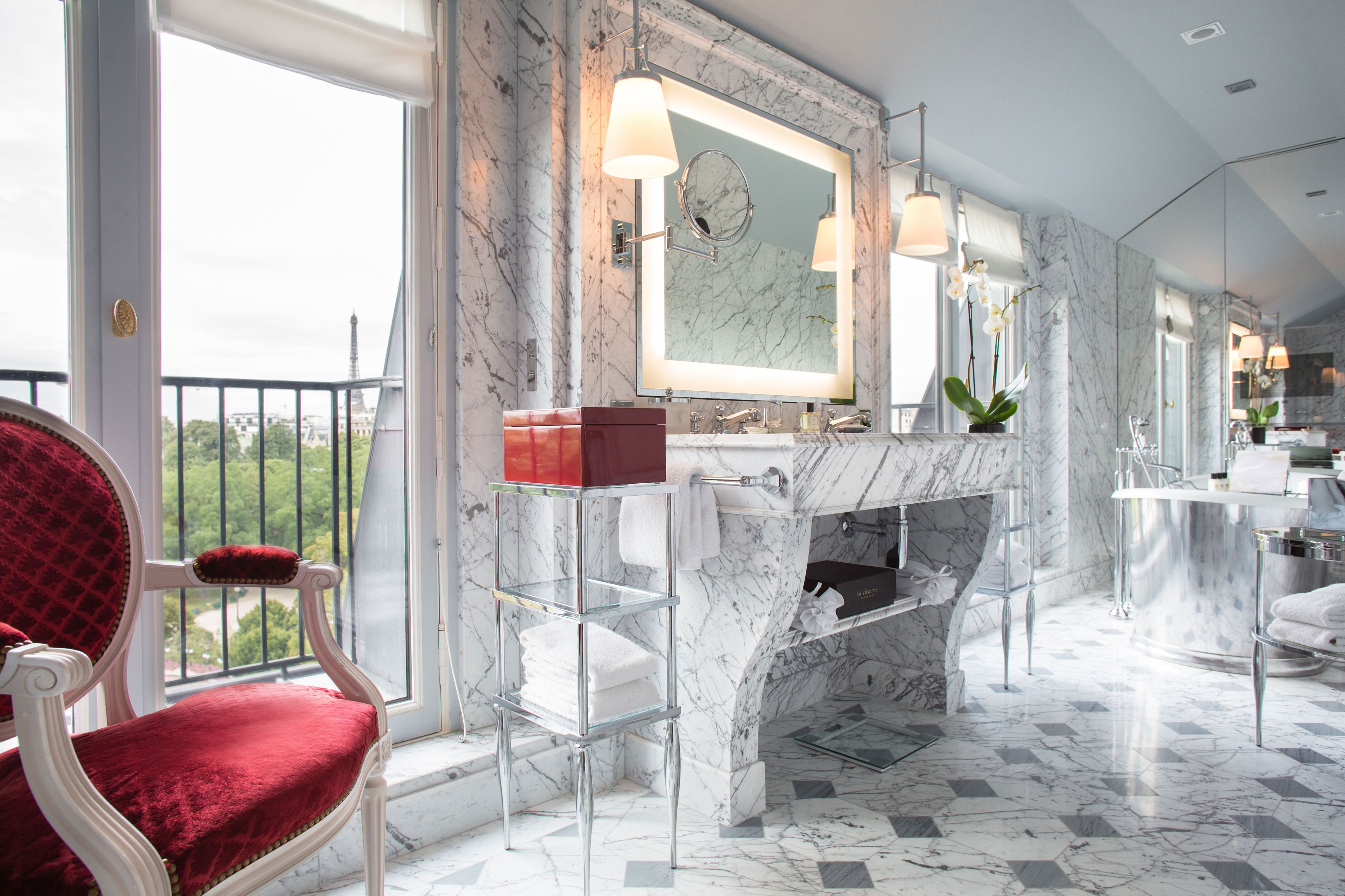 A spacious bathroom with a marble floor, a large mirror, and a red chair.