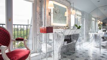 A spacious bathroom with a marble floor, a large mirror, and a red chair.