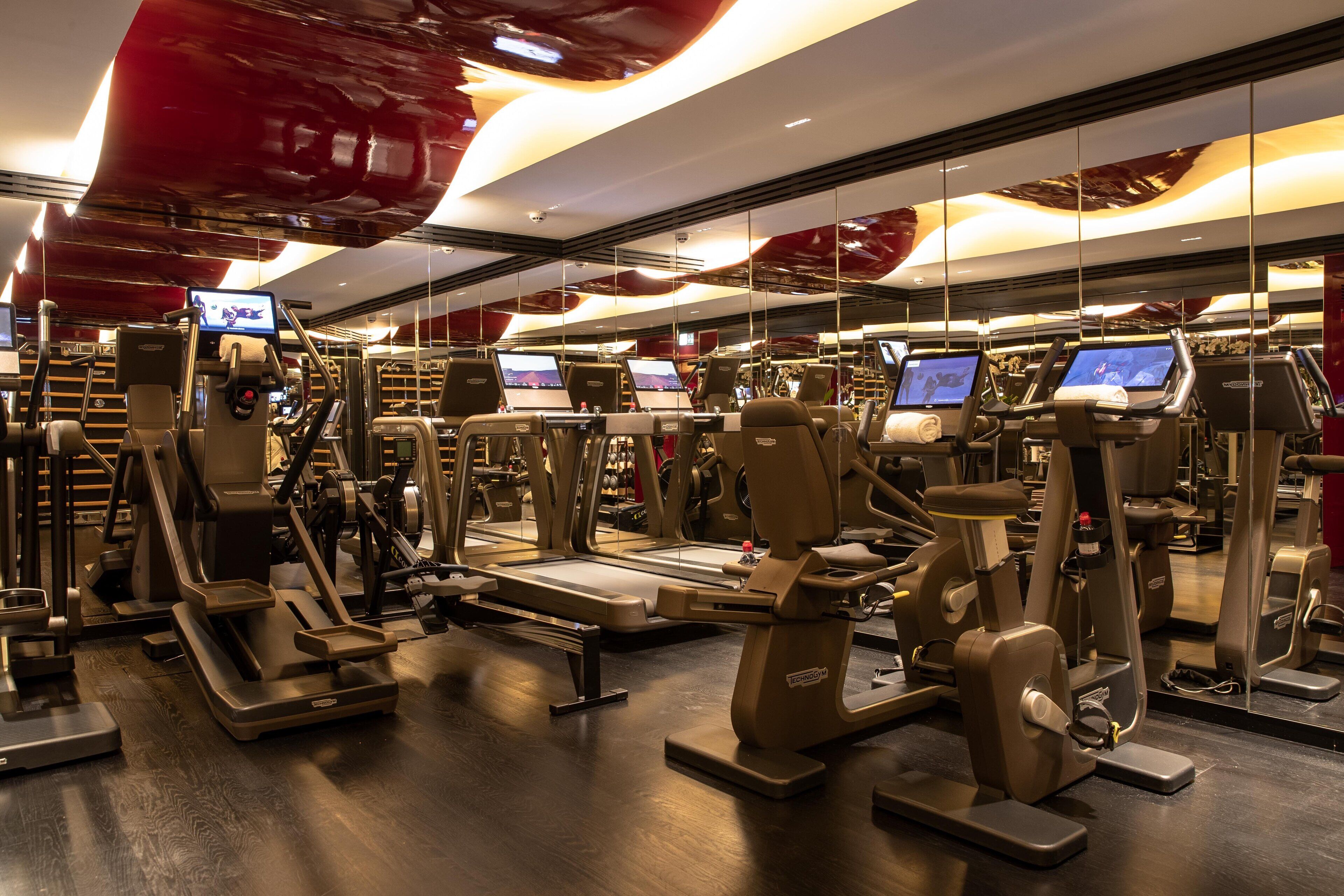 A modern gym with various exercise equipment, including treadmills and weight machines, and a large mirror wall.