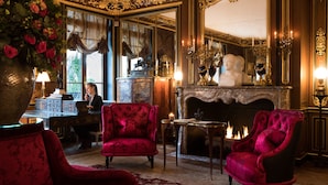 Een luxe kamer met weelderige inrichting, waaronder een openhaard, rode bekleden stoelen en een grote spiegel.