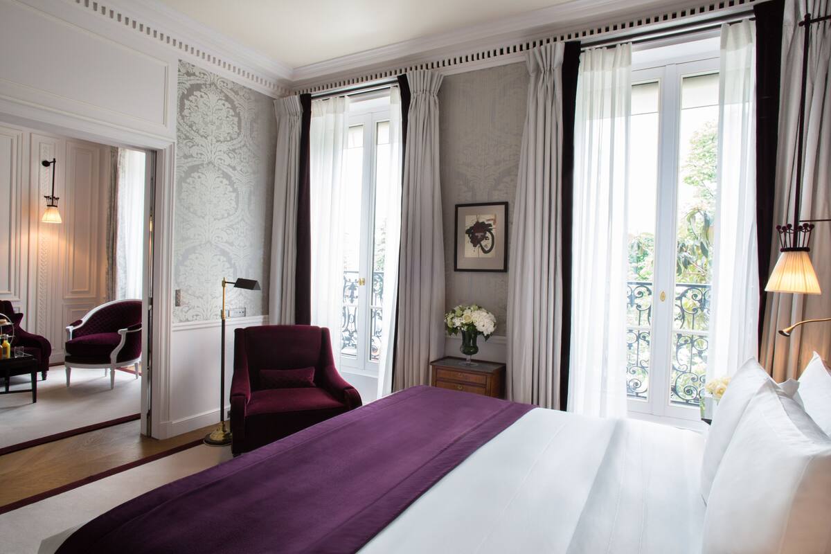 A hotel room with a bed, a chair, a nightstand, and a window with curtains.