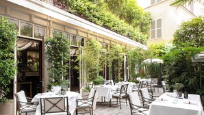 An outdoor dining area with tables and chairs, surrounded by lush greenery and a building facade. - La Reserve Paris Hotel and Spa (Paris)
