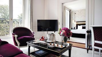 Una lujosa habitación de hotel con una cama grande, televisión, una mesa de comedor con un florero y un balcón con barandilla.