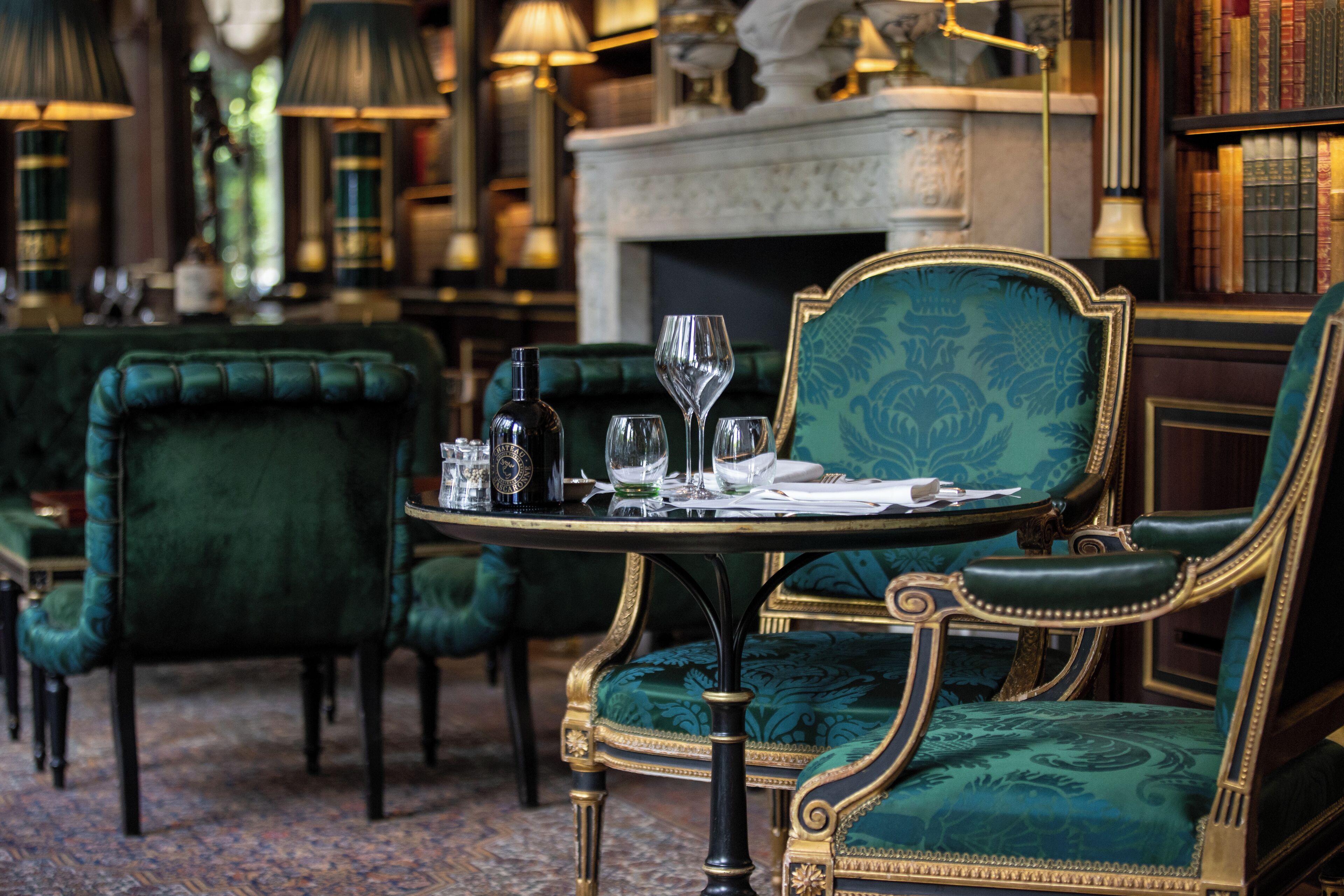 Un coin repas avec des chaises à revêtement vert, une table ronde sur laquelle se trouvent une bouteille, des verres et un menu.