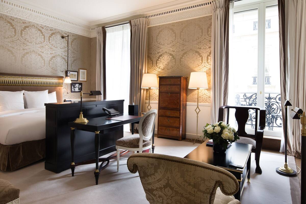 A hotel room with a bed, desk, chair, and a view of the city.