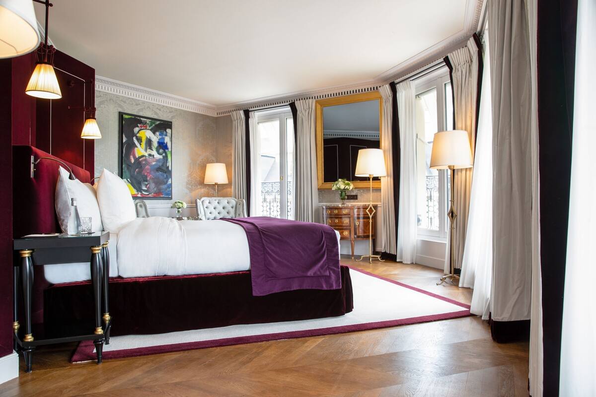 A hotel room with a bed, bedside tables, a desk, a chair, and a window with curtains.