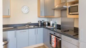 Una cocina moderna con armarios grises, un lavamanos de acero inoxidable, un microondas y un reloj en la pared.