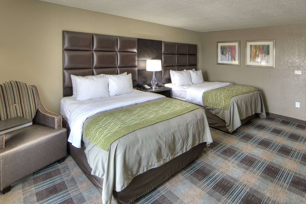 A hotel room with two beds, a chair, a nightstand, and a lamp.