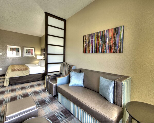 A hotel room with a sofa, a bed, a chair, and a painting on the wall.