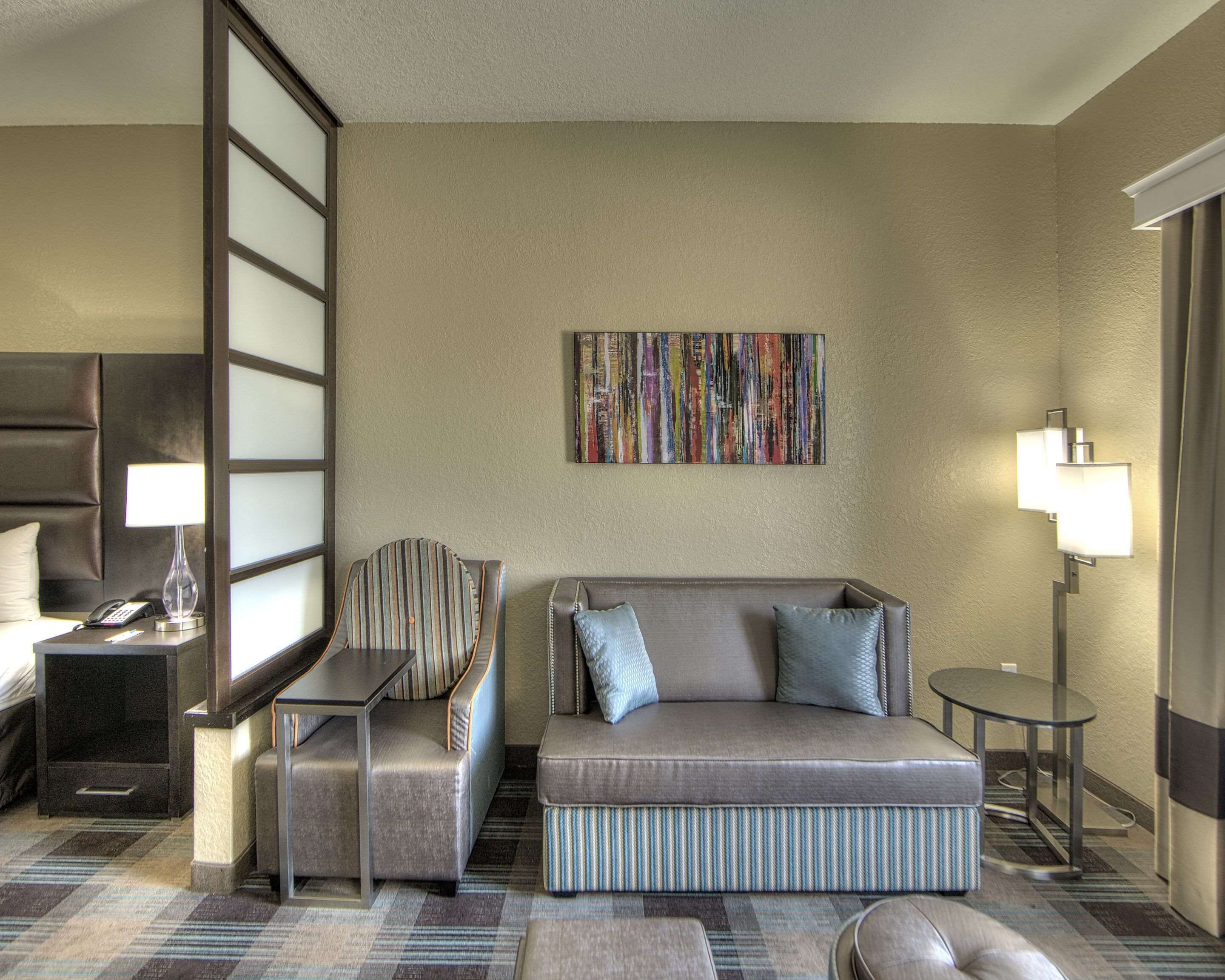 Een hotelkamer met een bank, fauteuil, bijzettafeltje, lamp en een schilderij aan de muur.